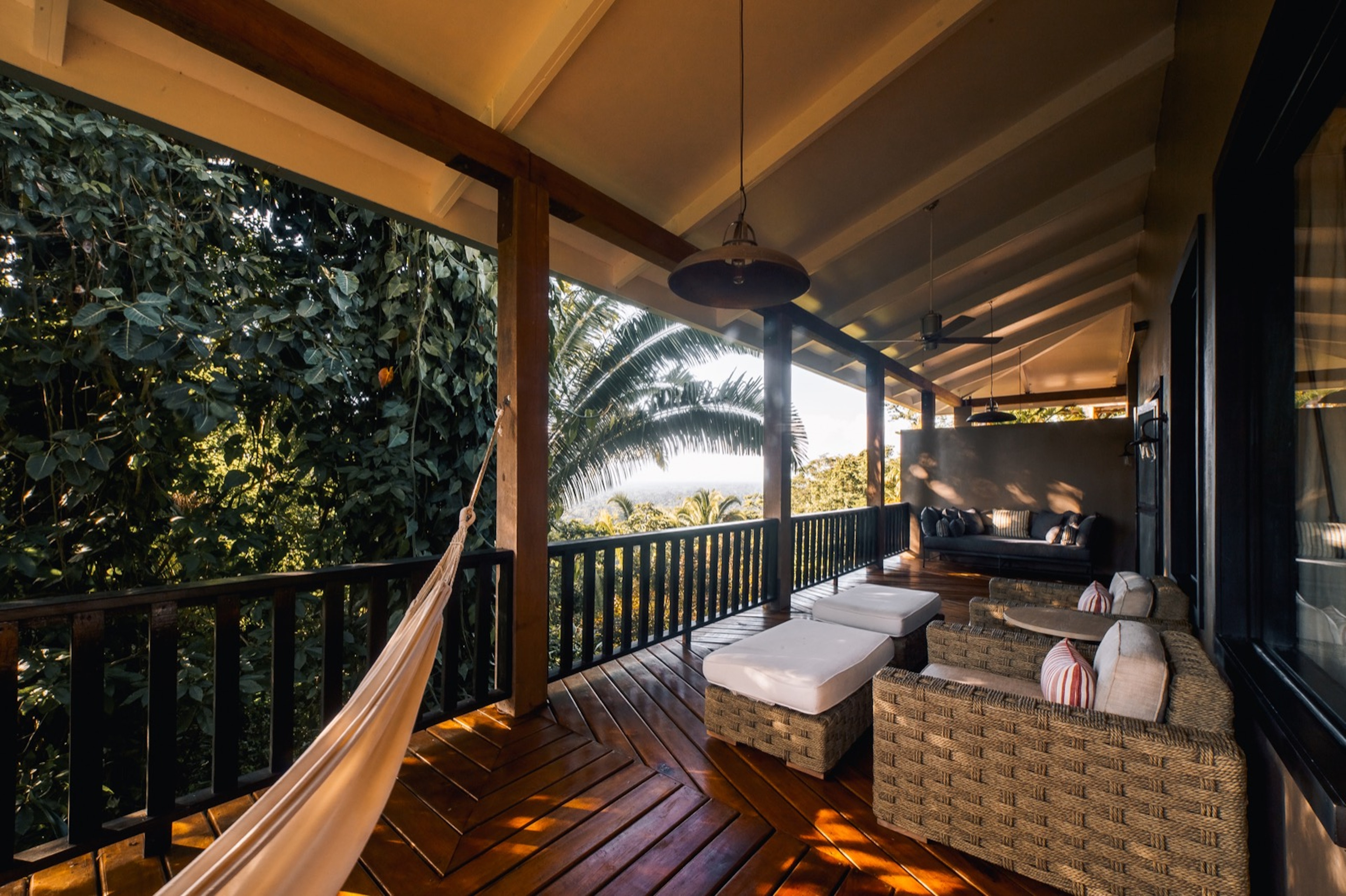 A hammock is tied to the side of a terrace, while a pair of chairs and a sofa fill the rest of the space on the wooden terrace; eco luxury resorts