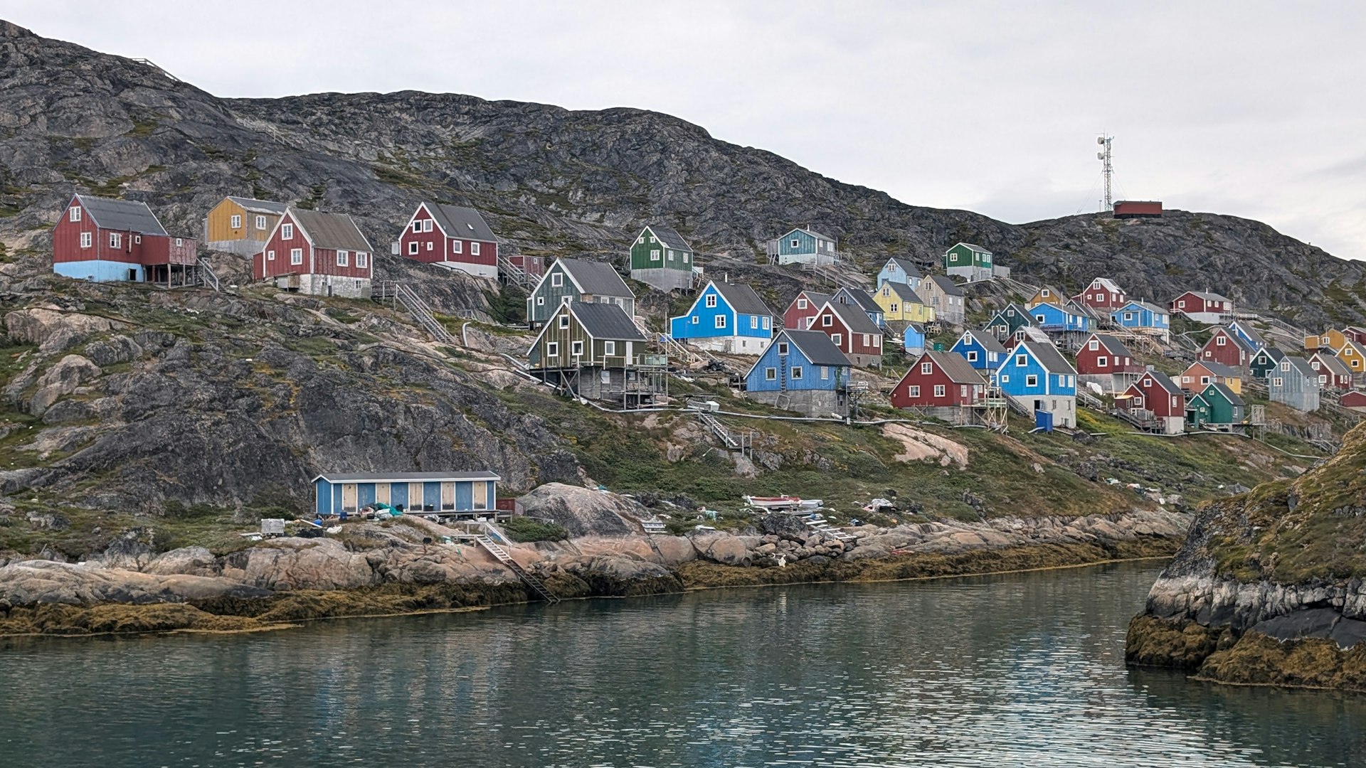 A series of colorful wooden houses built into the side of the cliff viewed from a ferry