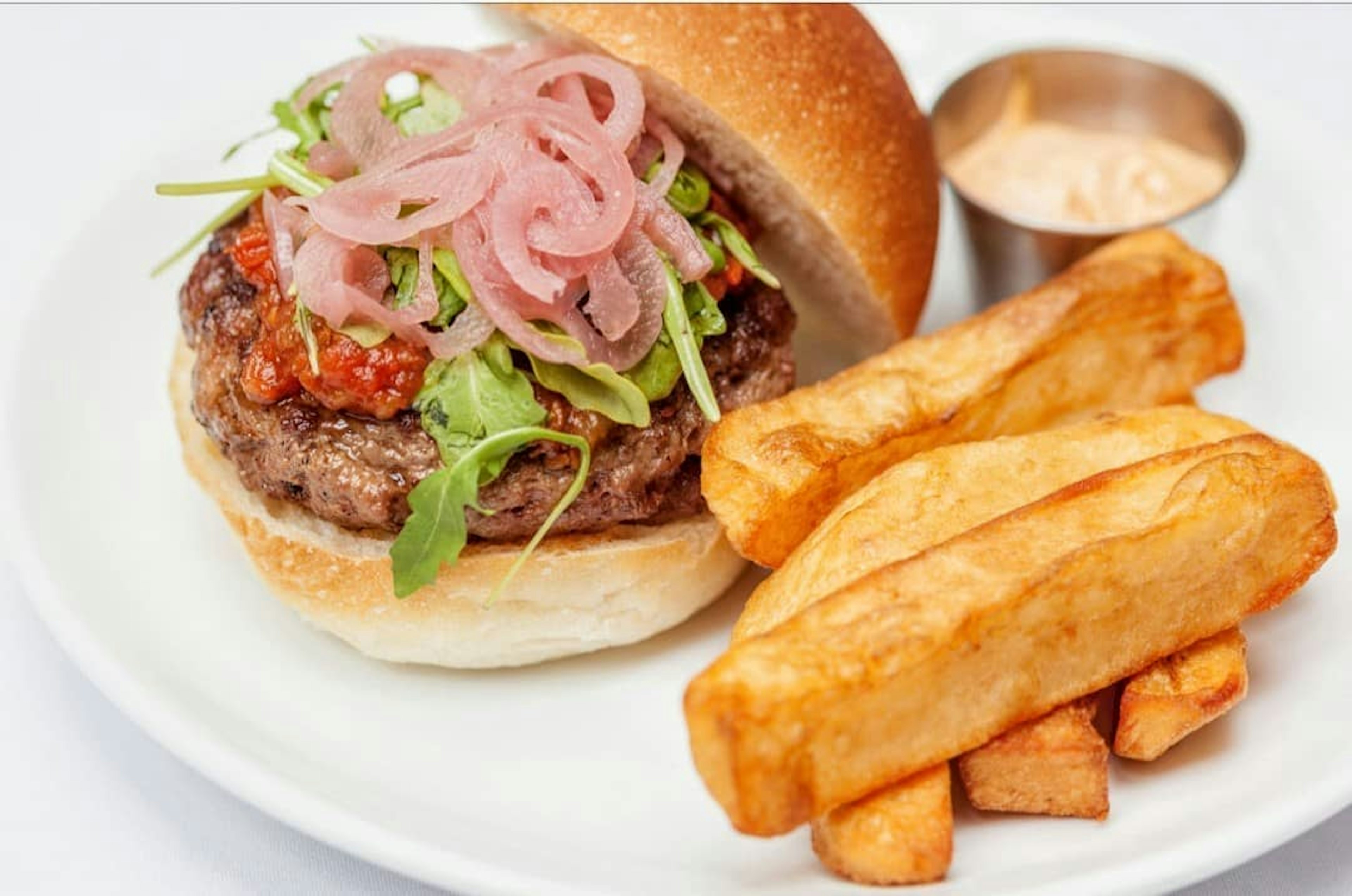 Closeup of a Kangaroo burger topped with sauce, greens and onions and a side of french fries