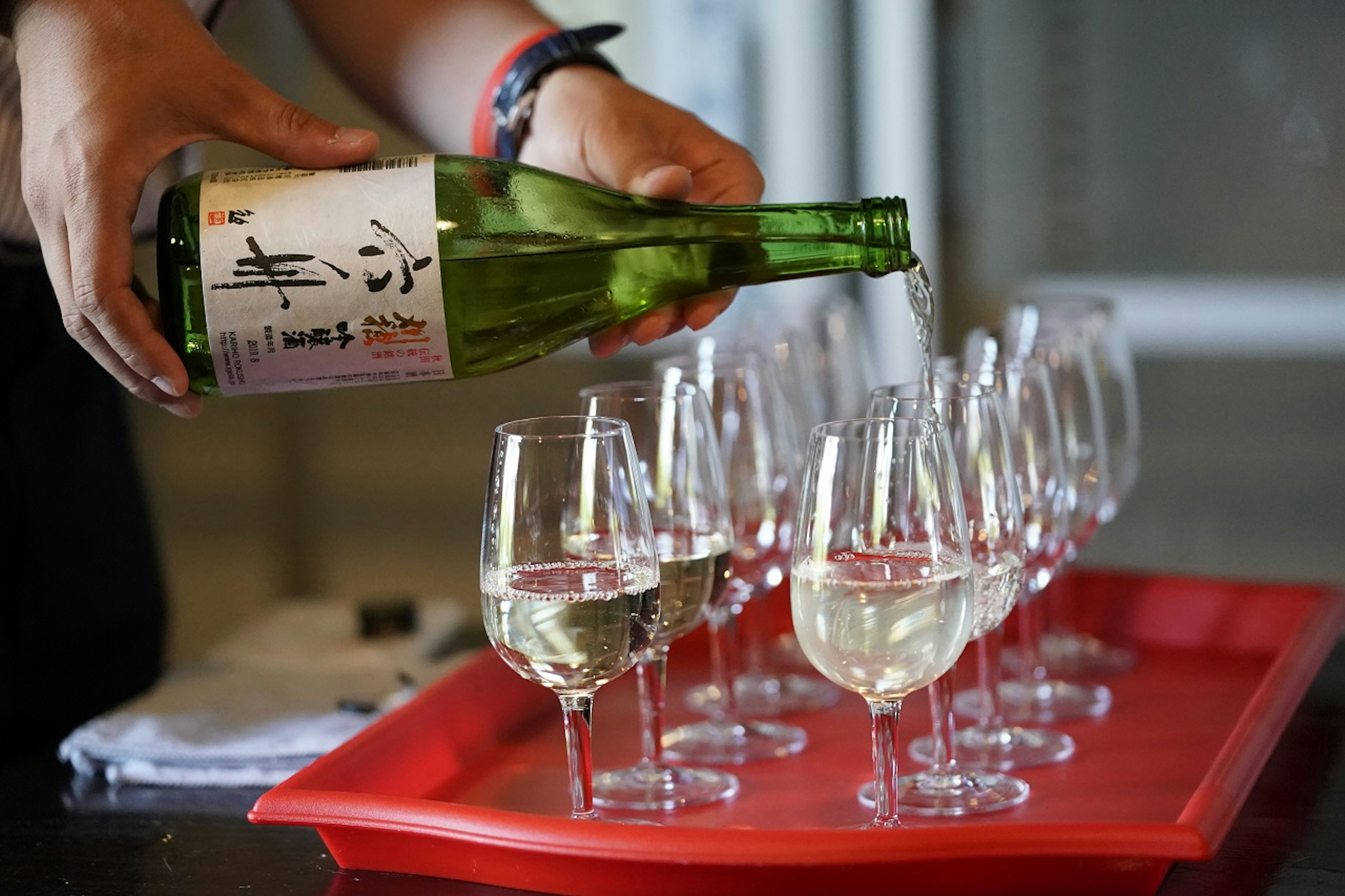 Sake is poured into glasses on a red tray