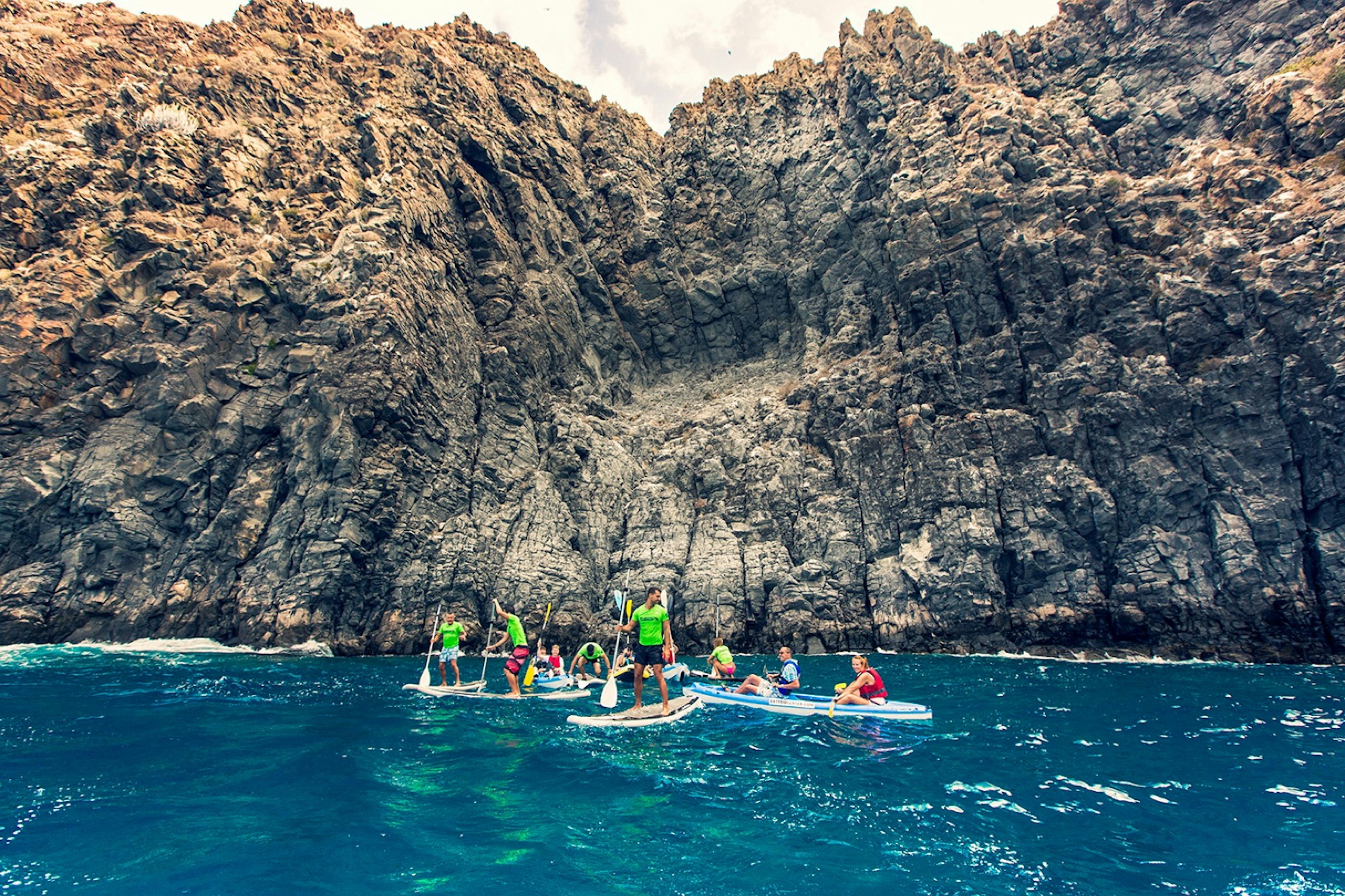 A group of kayakers paddle next to a large rock formation in Tenerife.