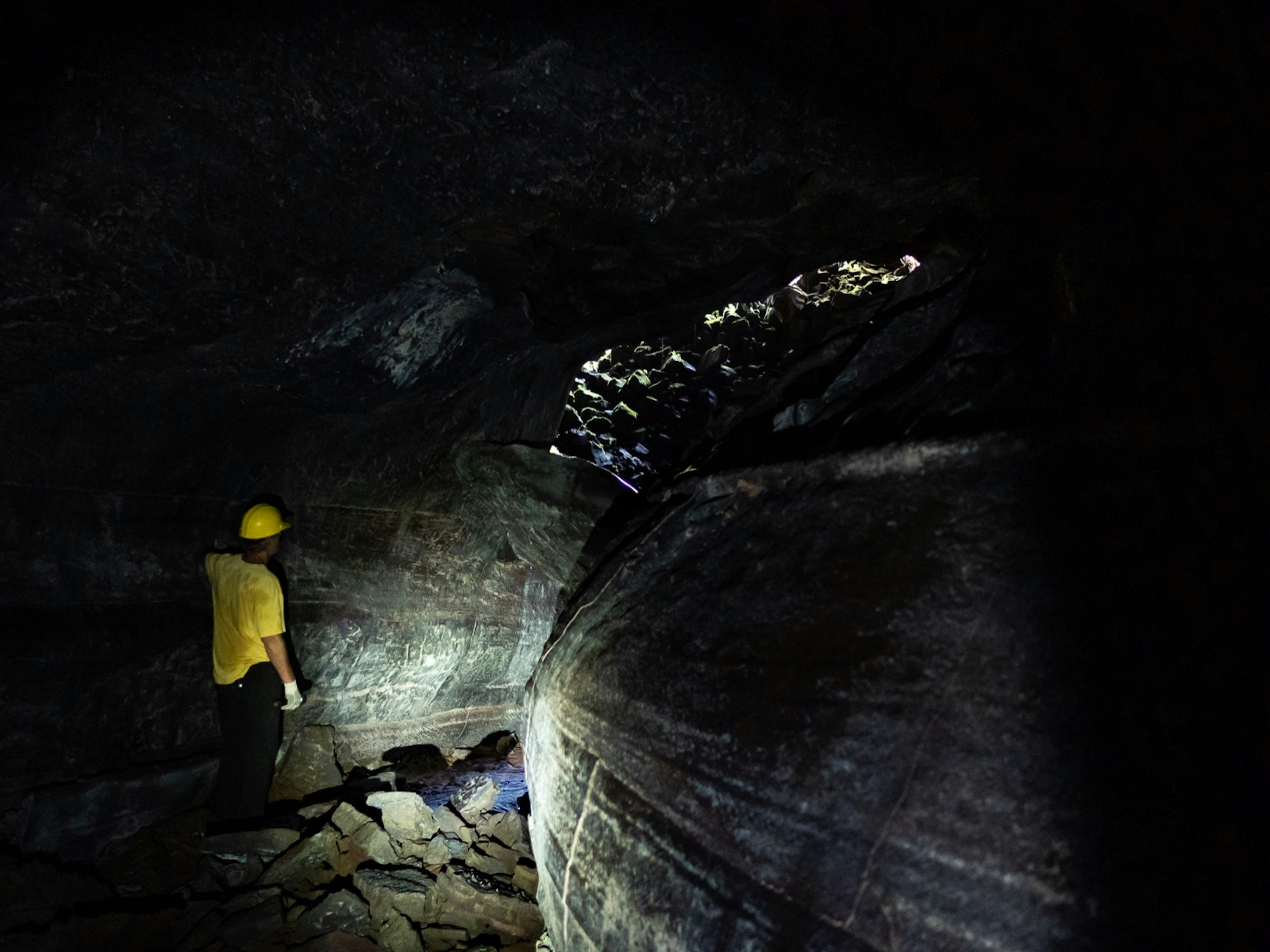 A man walks through a dark cave as his flashlight highlights an array of different colors on the wall