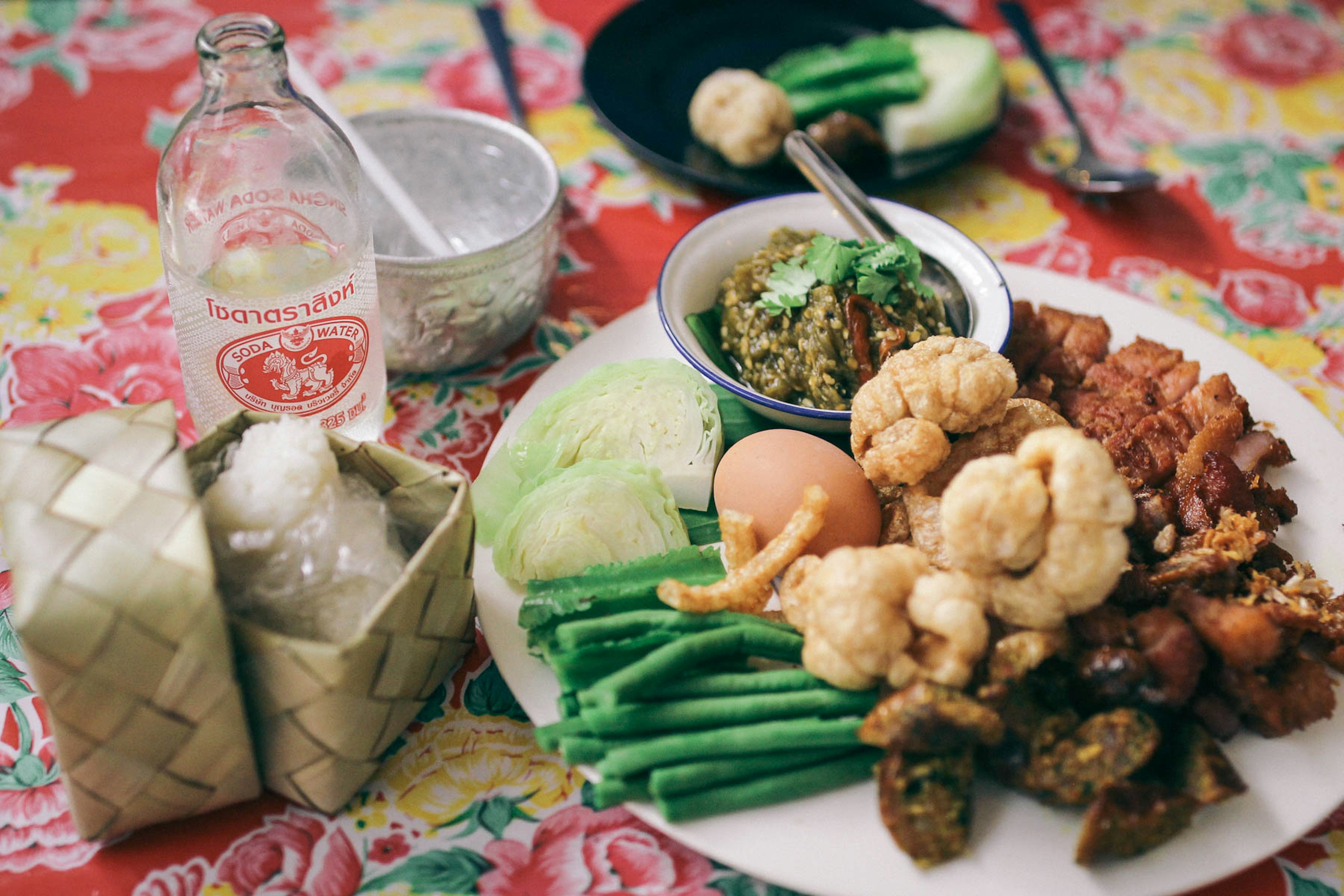 A plate of food, consisting of pork, egg, vegetables and green nam prik num dipping sauce, sits on a colourful tabletop in Kinlum Kindee restaurant