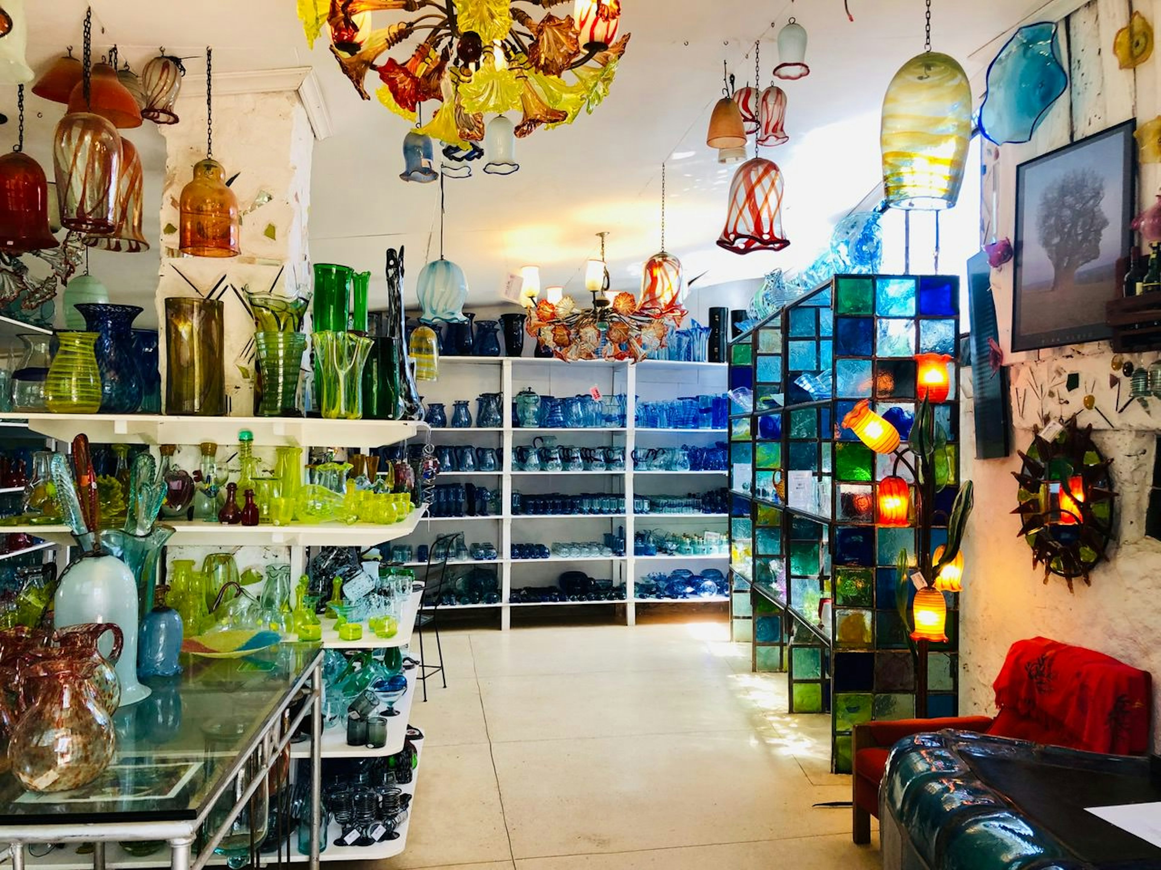 A shop with a white floor and white shelves stacked with hundreds of colourful, hand-made glass vases, ornaments and tablewear