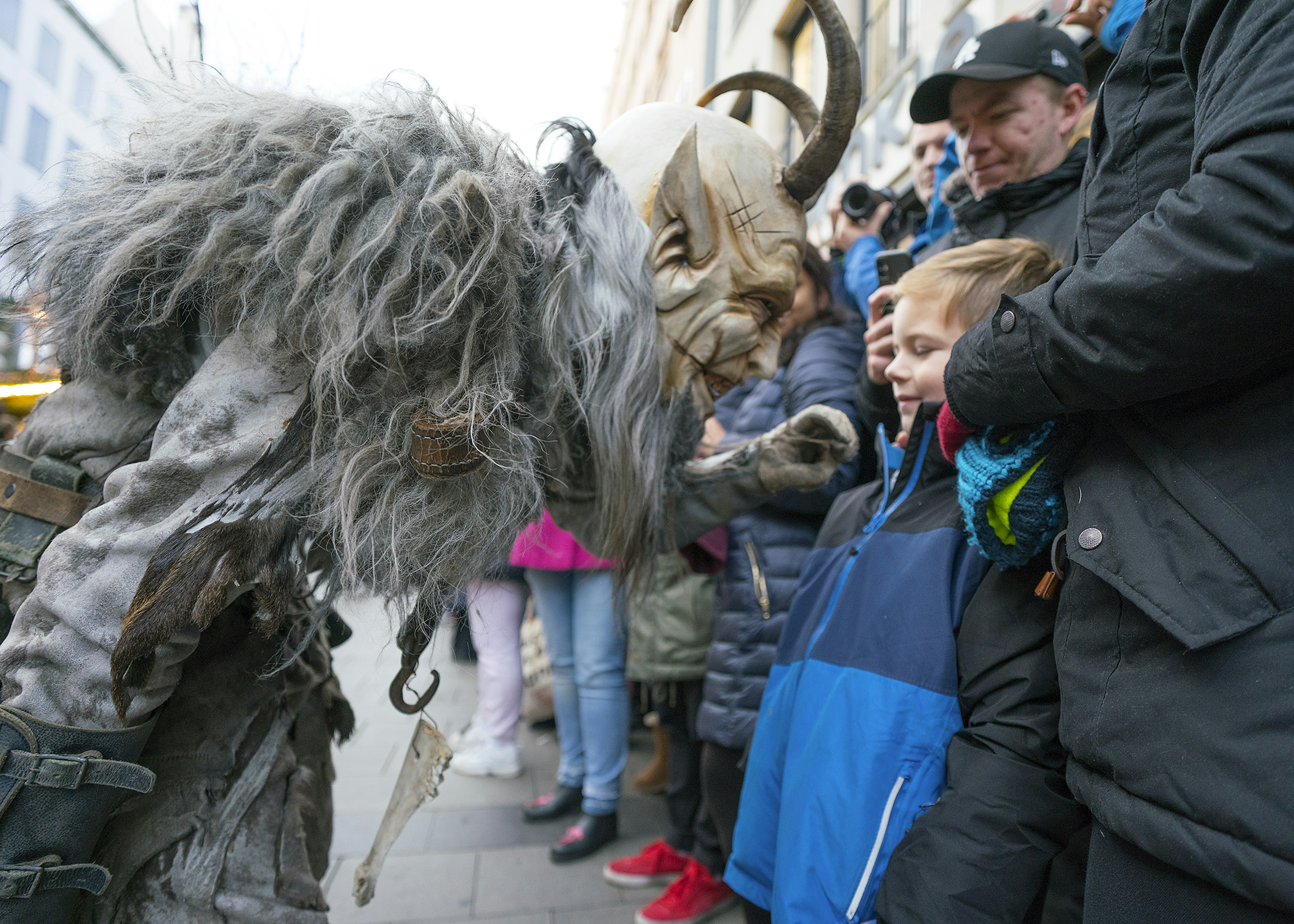 A Krampus character gets in the face of a child who smiles hesitantly back