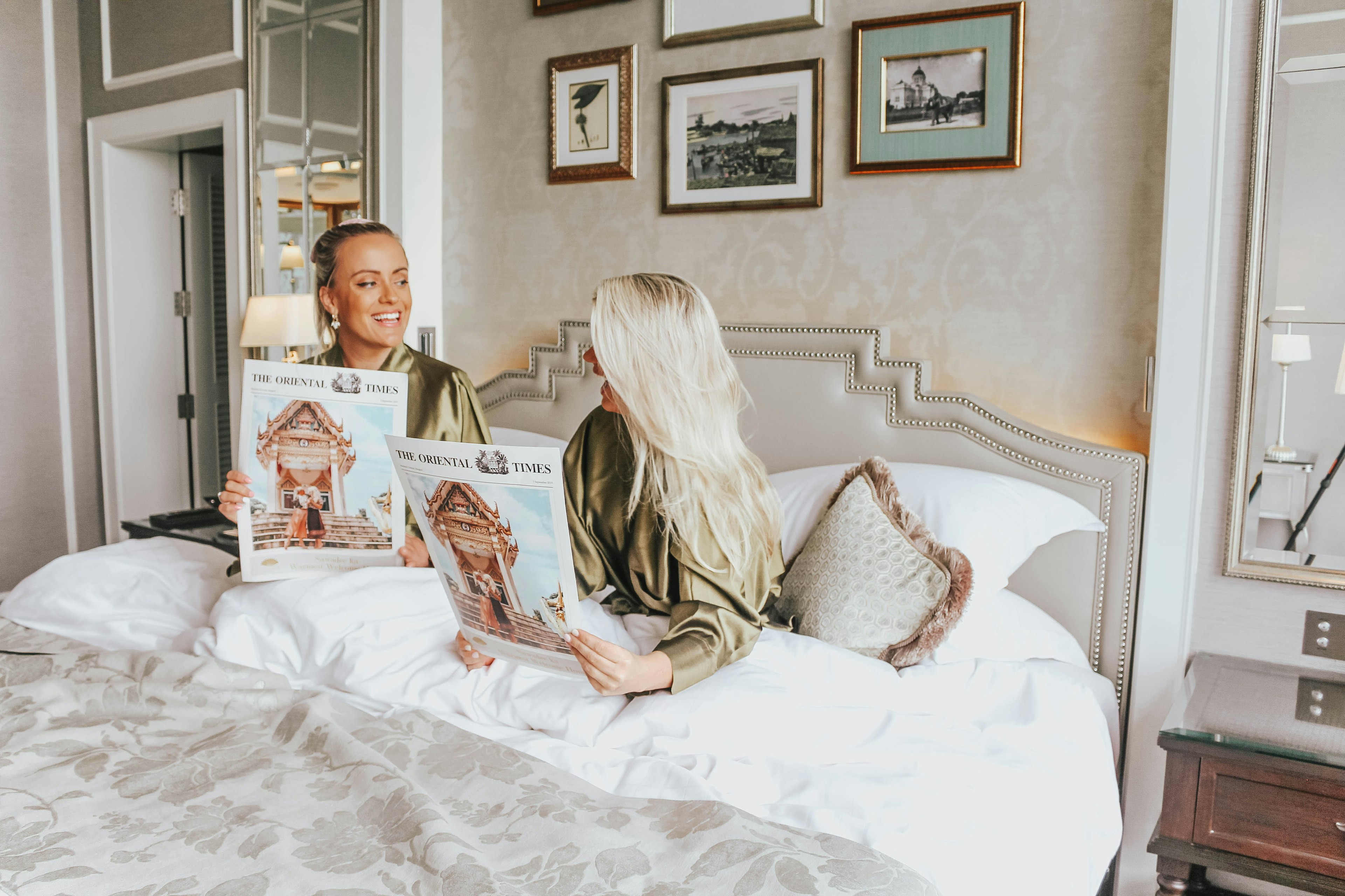 Whitney and Megan sitting reading a hotel 'newspaper' in bed at the Mandarin Oriental in Bangkok, Thailand.