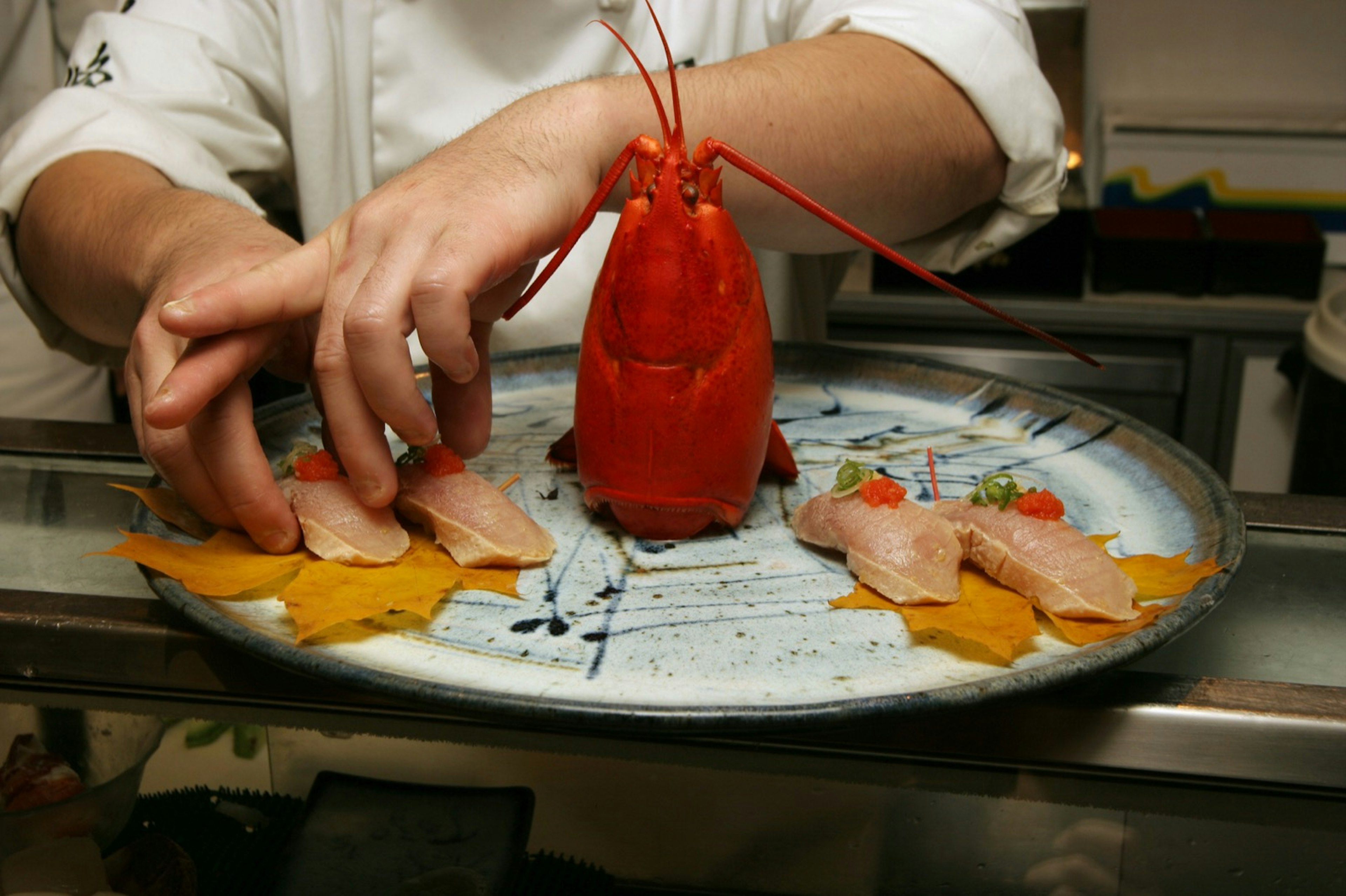 A chef preparing a plate of nigiri surrounding a large lobster head; California roll