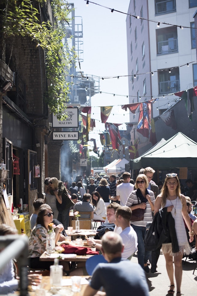 Diners sit on outside benches on one side of an alley, with traders' stalls lining the walls on the otherside