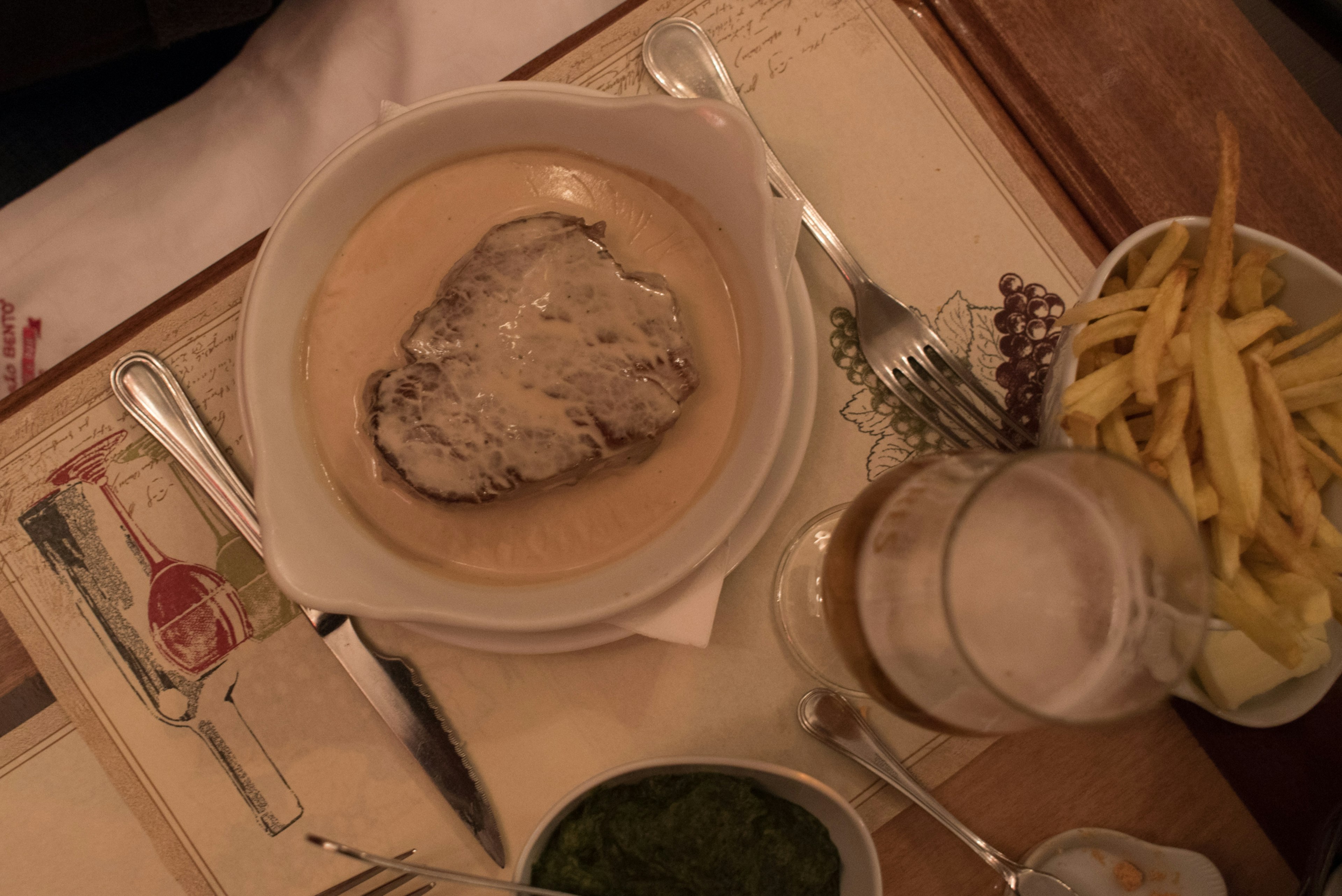 A flat lay shot of a dinner table with a dish of steak smothered in a creamy sauce with chips and beer on the side