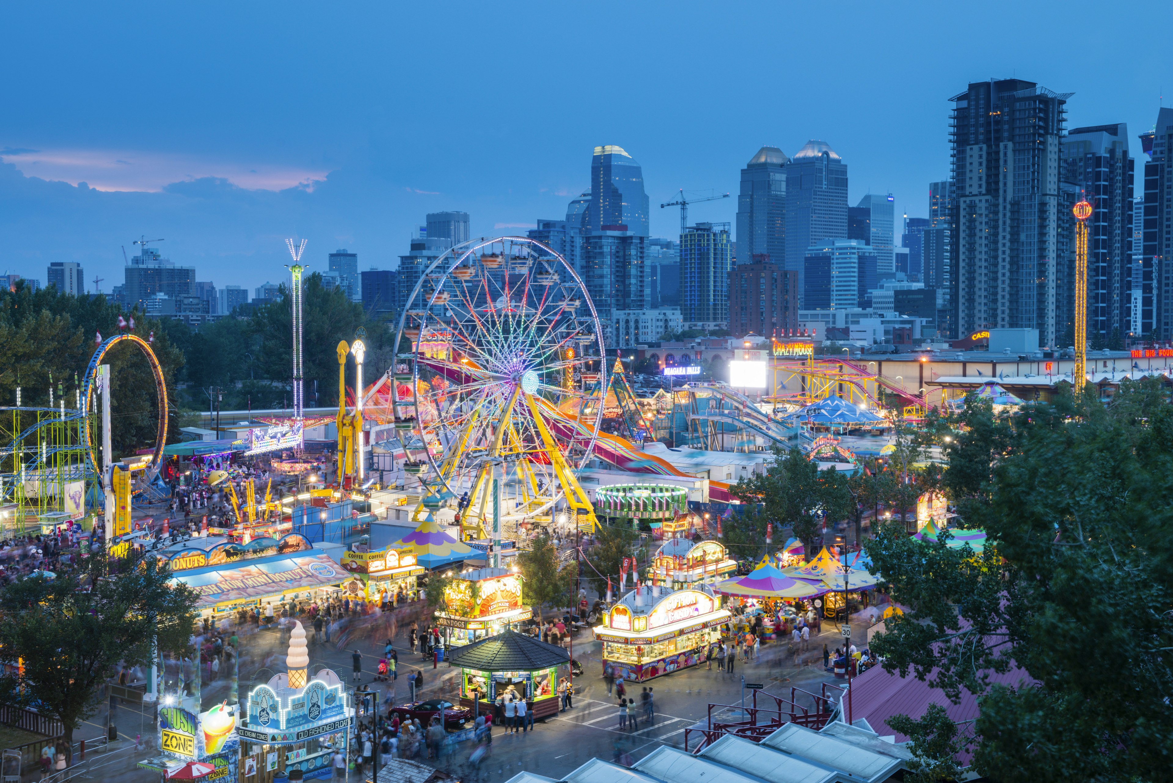 A fun fair with a Ferris wheel lit up at night at a busy event in a city