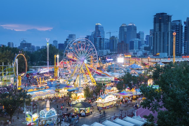 A fun fair with a Ferris wheel lit up at night at a busy event in a city
