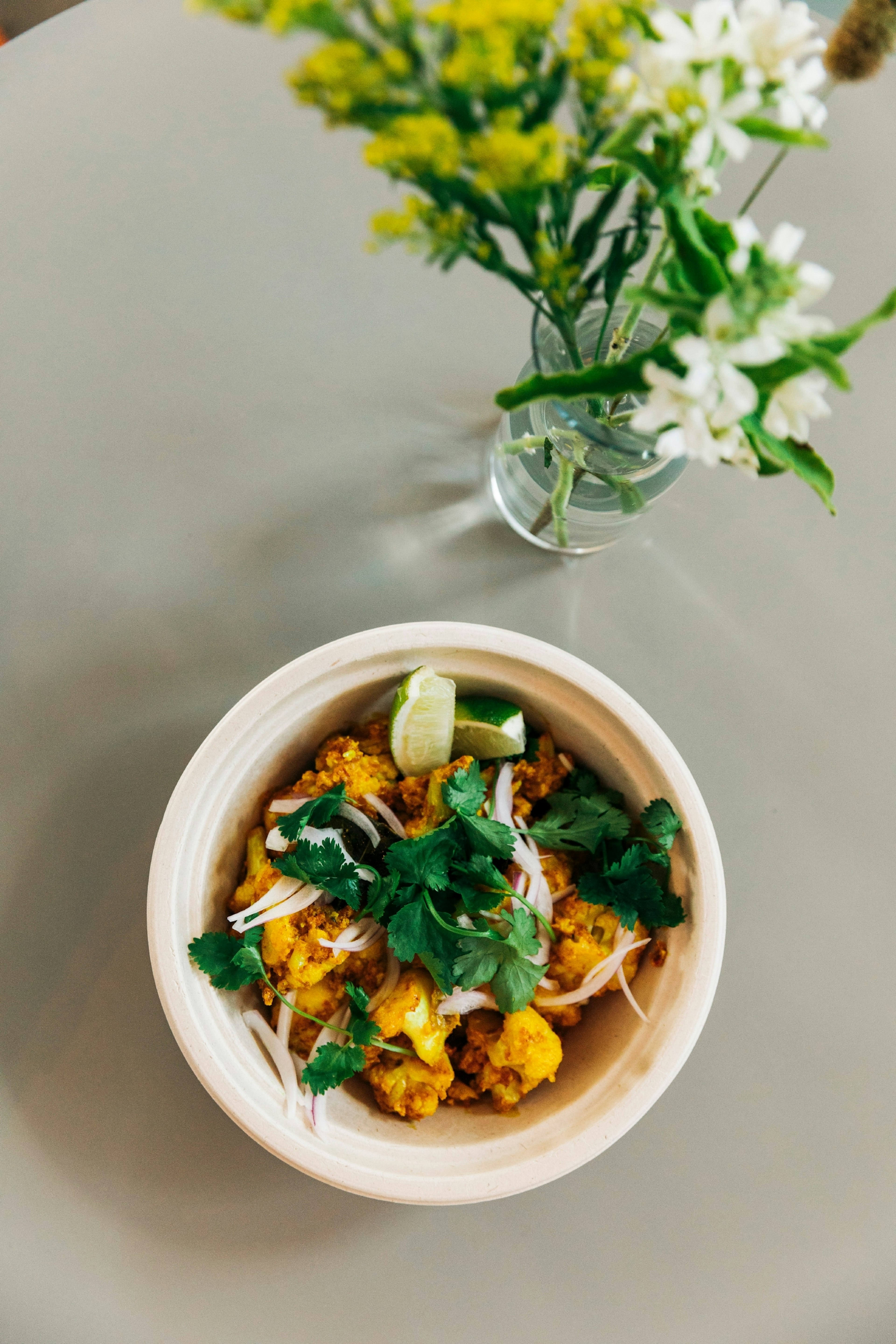 A dish of fried spiced cauliflower with an onion and cilantro garnish