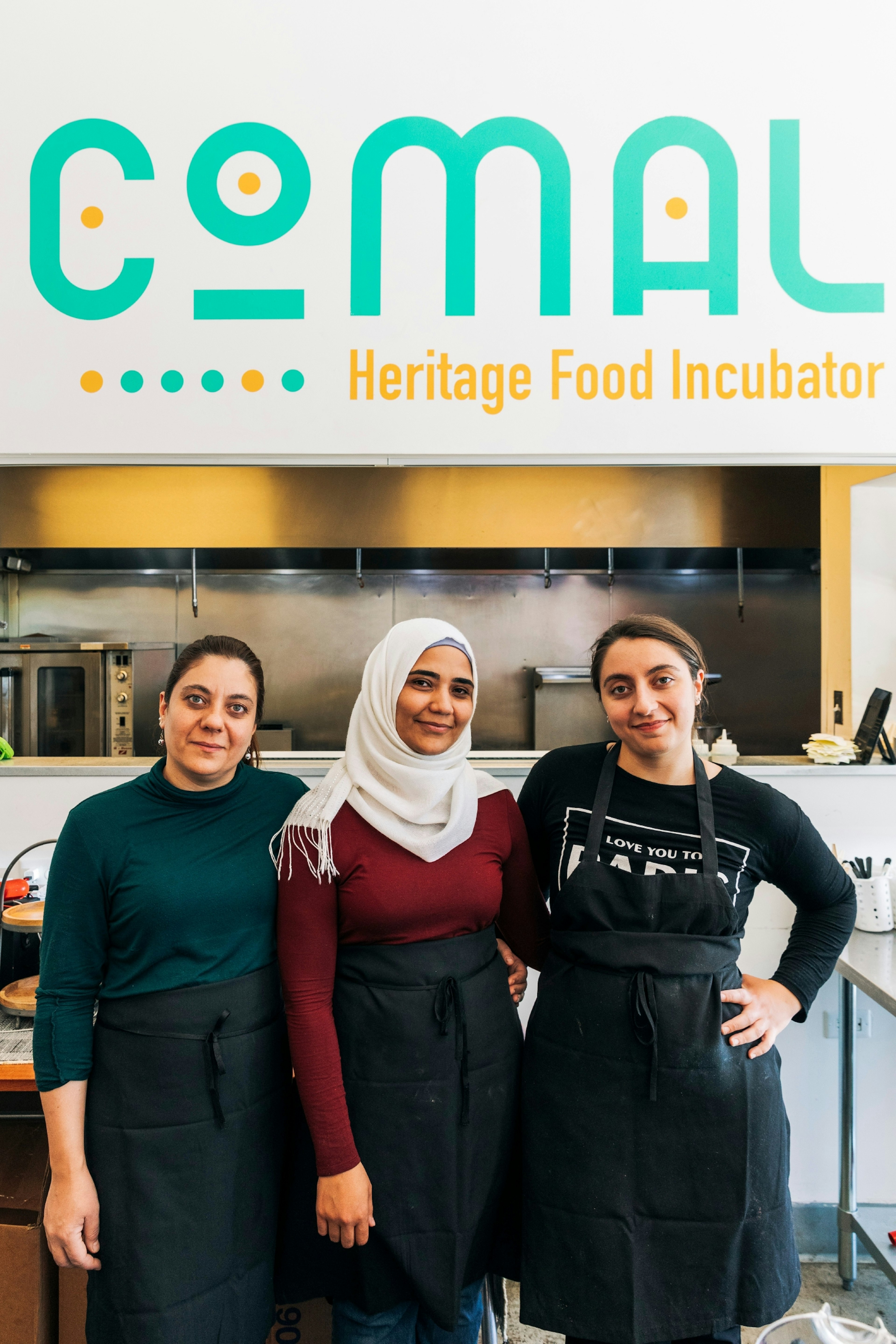 Three women pose for a photo beneath the Comal sign