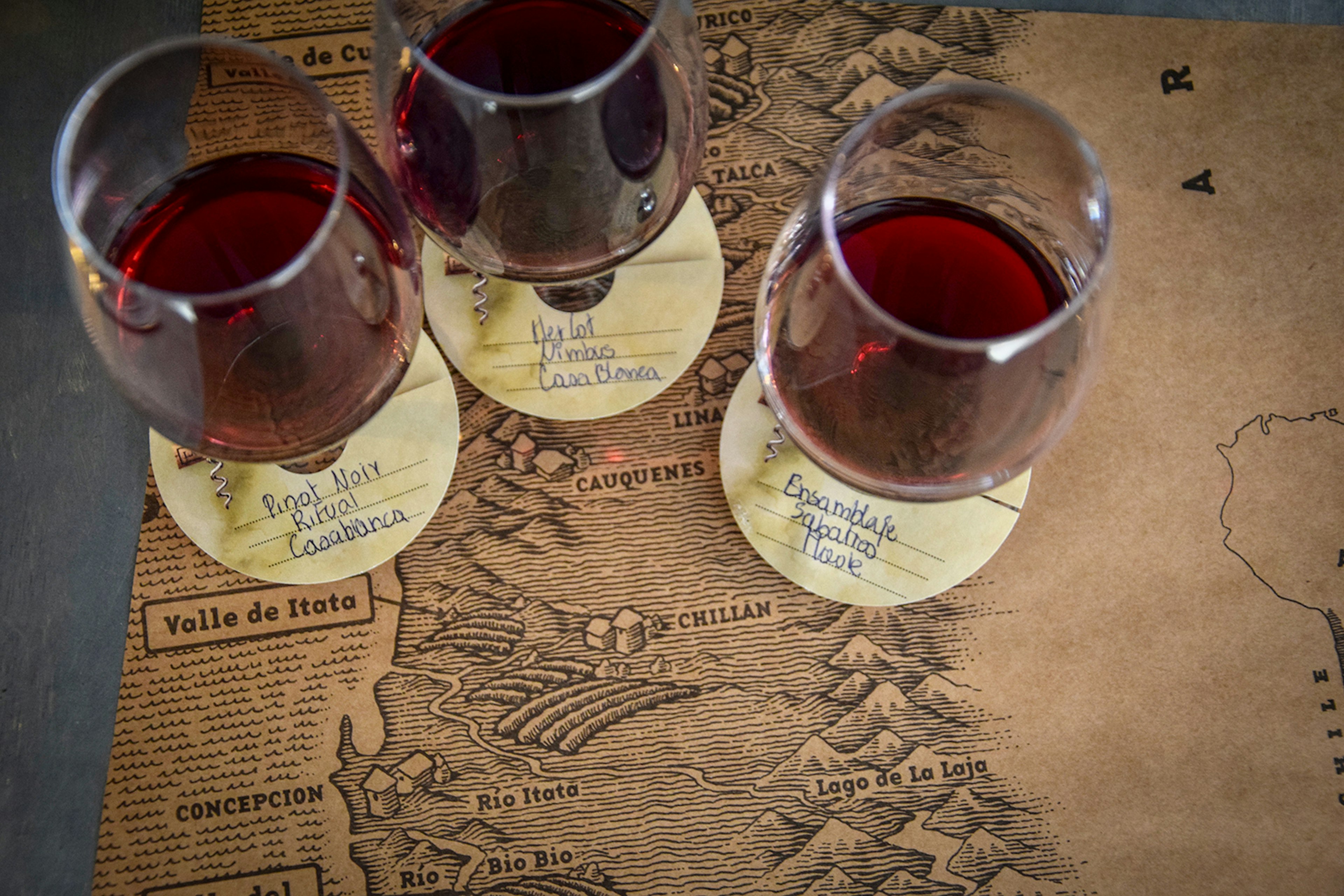 An overhead shot of three classes of red wine placed on a map of Chile