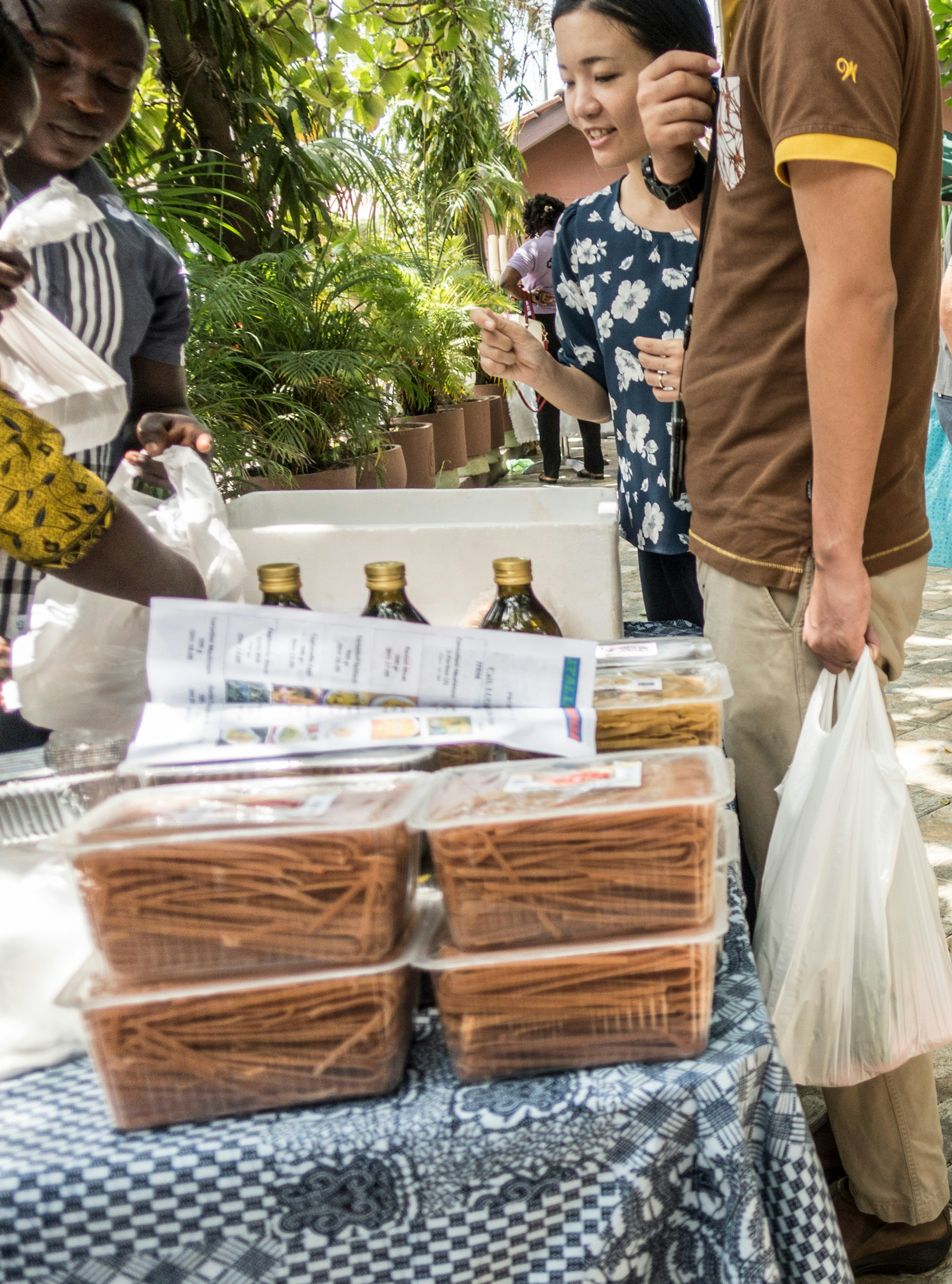 A man, with a plastic bag full of produce haning from his hand, stands with a woman at a stall within Labone Green Maket © Elio Stamm / ϰϲʿ¼