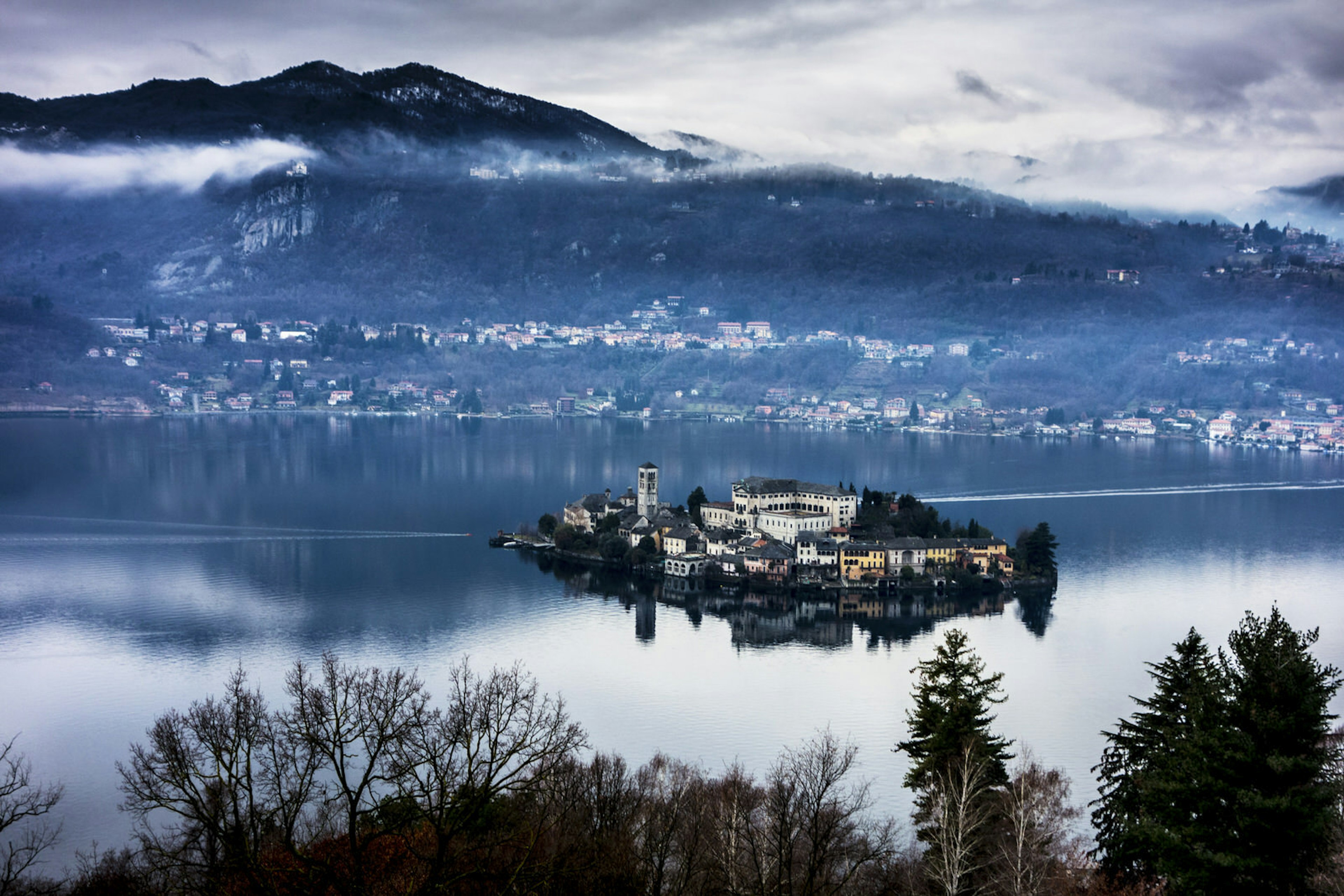 Isola San Giulio, packed with historic buildings, sits in the middle of Lake Orta, with mountains rising behind © Francesco Meroni / Getty Images