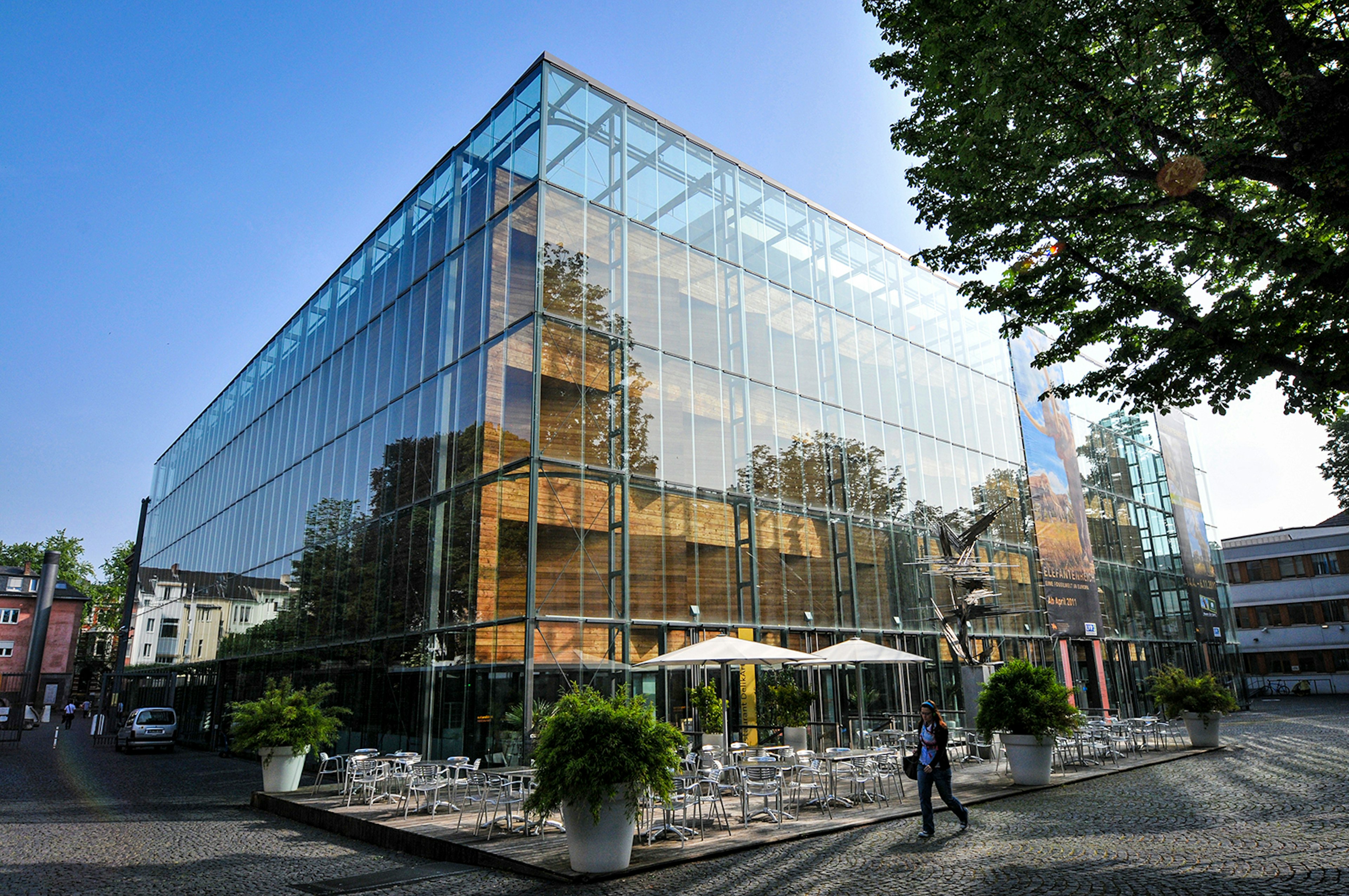 Building with a glass outer shell and umbrellas on a patio in front