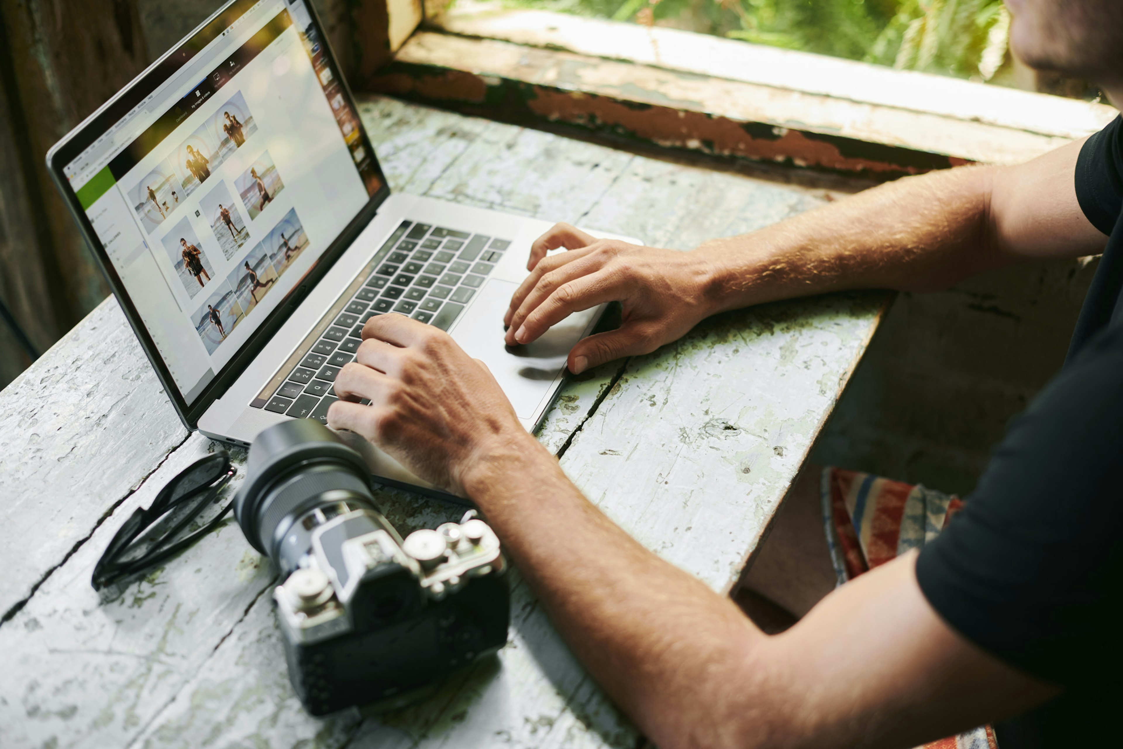 A man on a laptop is looking at photos as his camera sits on a table next to him