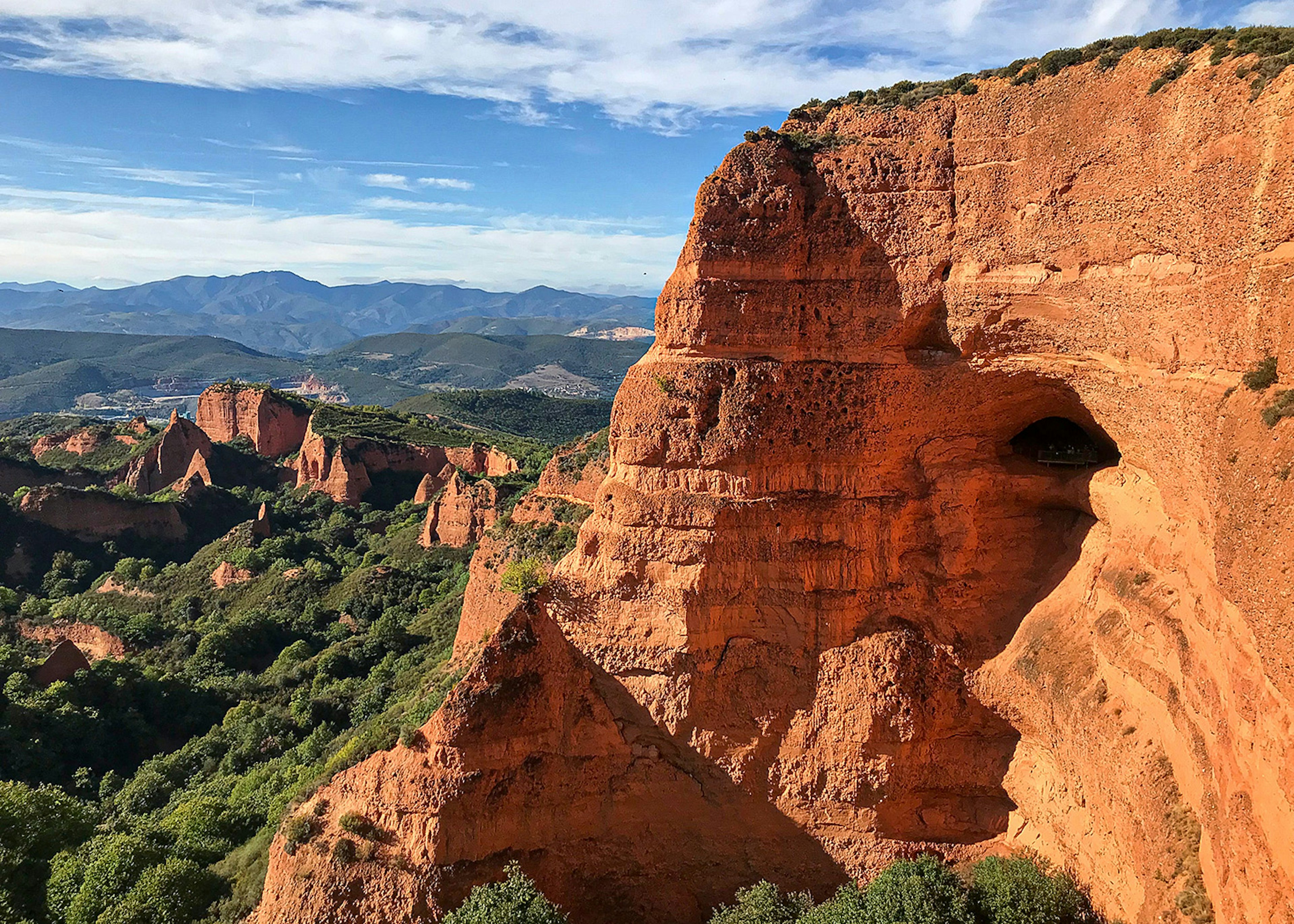 Striking orange cliffs, capped with greenery, roll towards a mountainous horizon in this rugged view of the Castilla y Leon region in Spain