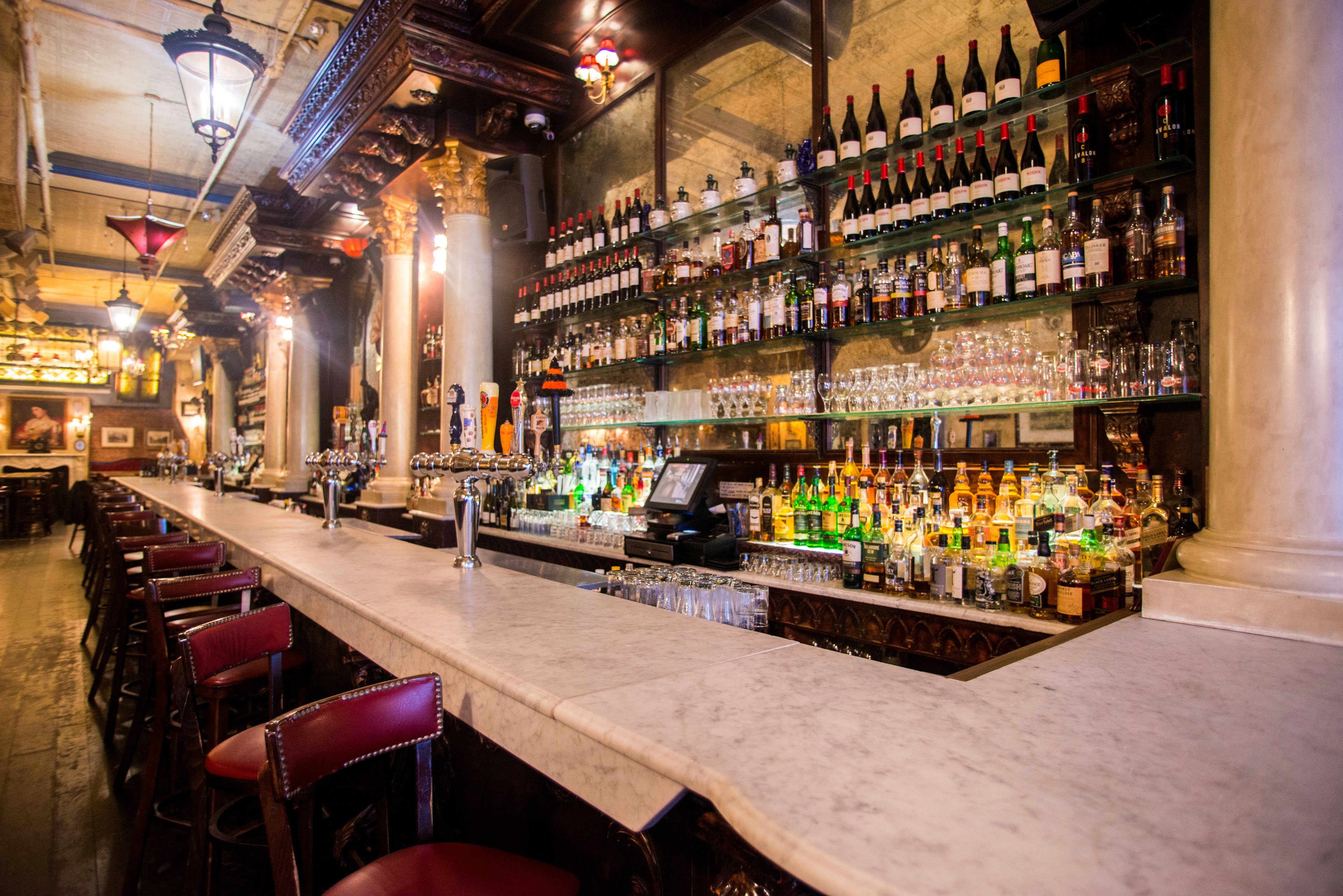 The light colored stone bar at Lillie's Victorian Establishment. Behind the bar are rows of glass shelves lined with wine and spirit bottles.