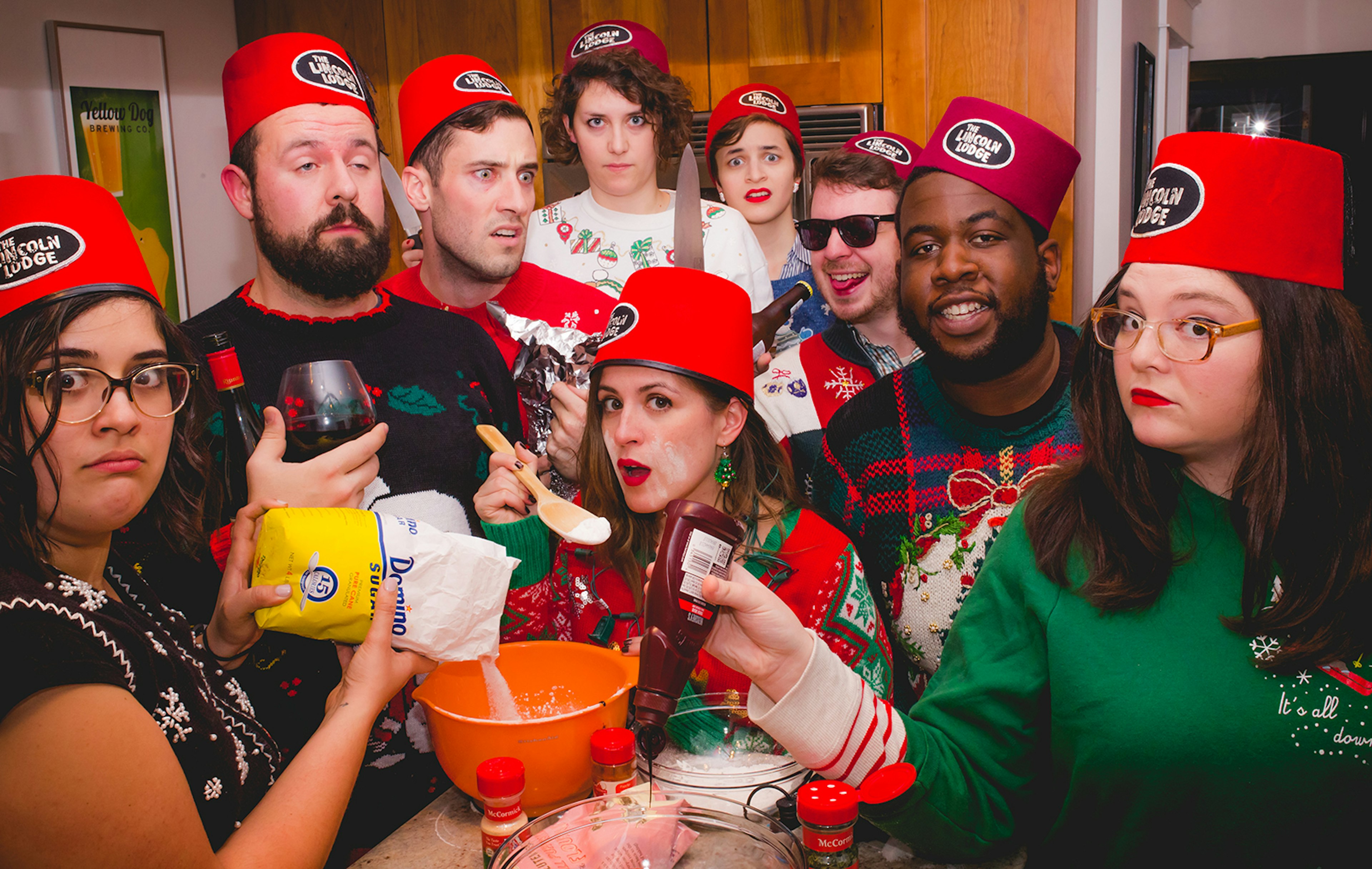 group of comics in red hats pour ingredients into a bowl as part of a comedy skit