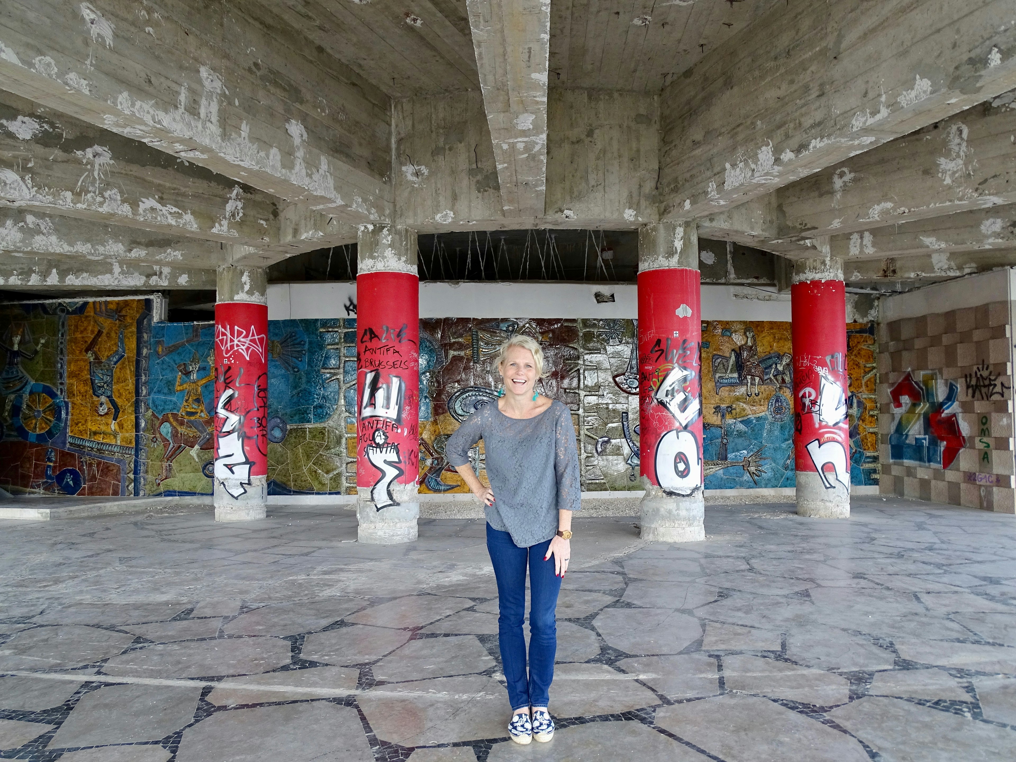 A woman poses smiling in front of graffitied columns in the Miradouro Panoramico de Monsanto, Lisbon.