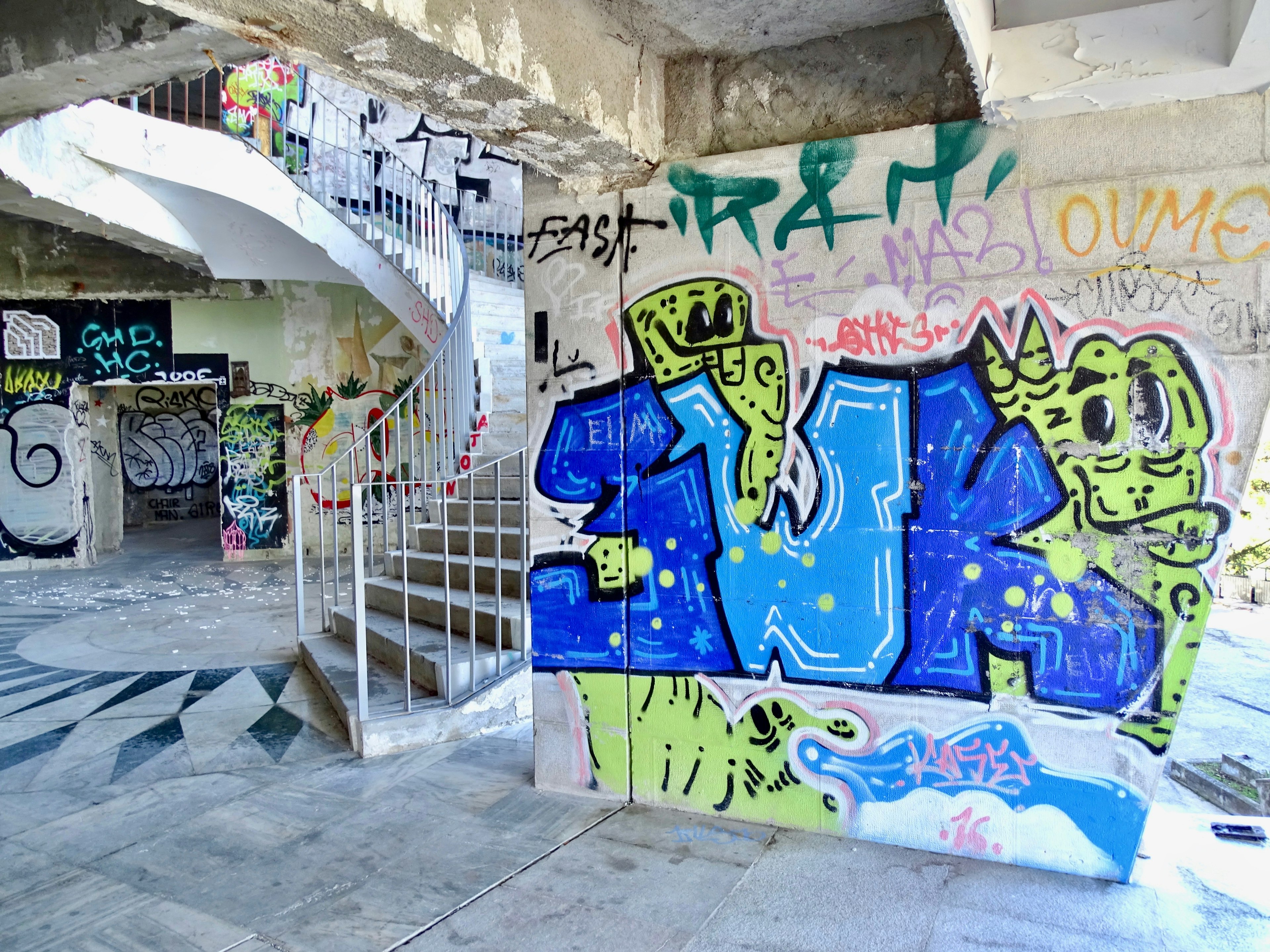 A concrete spiral staircase bordered by graffitied walls in the Miradouro Panoramico de Monsanto, Lisbon.