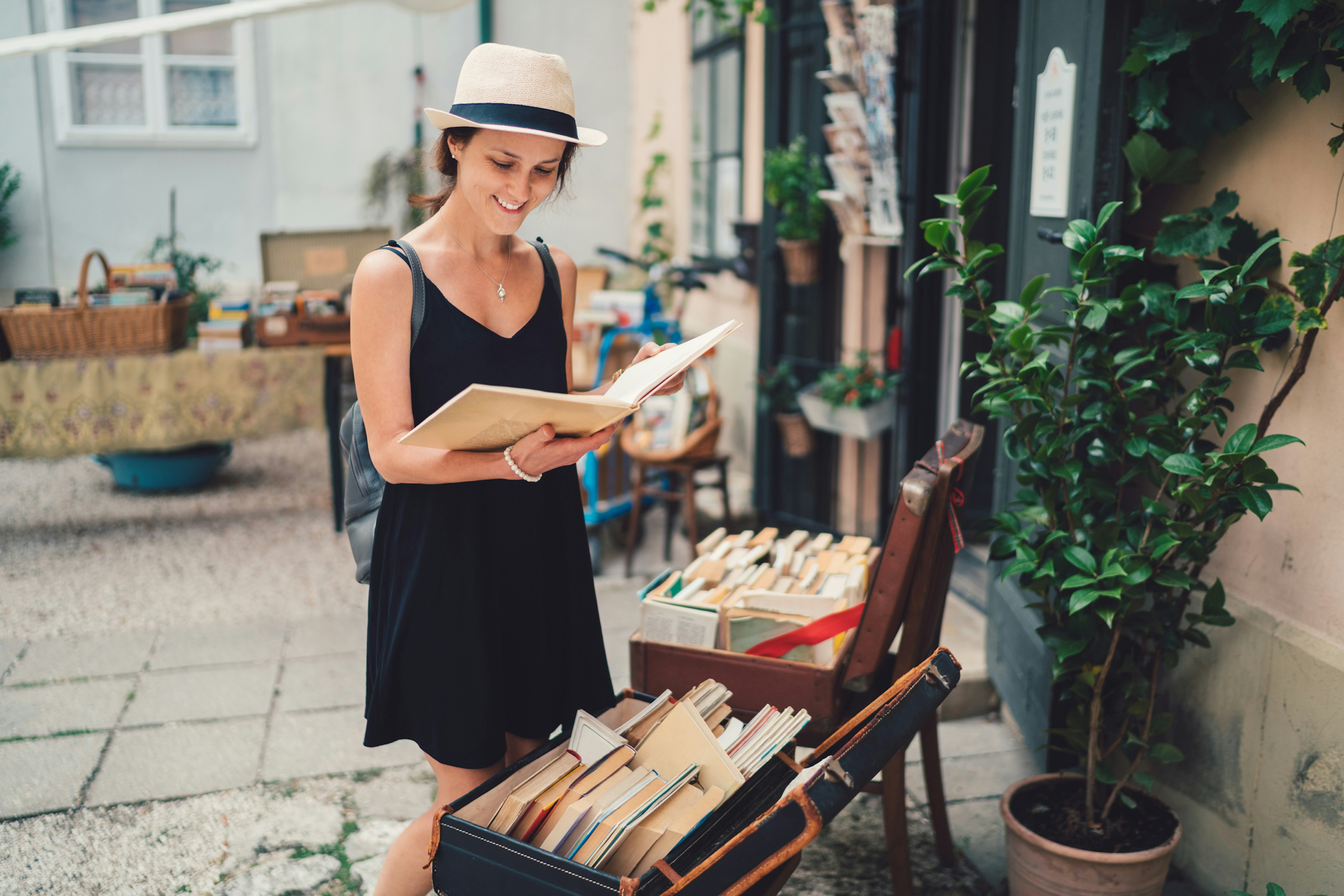 A woman leafs through a book while standing in front of a suitcase filled with books; national book month