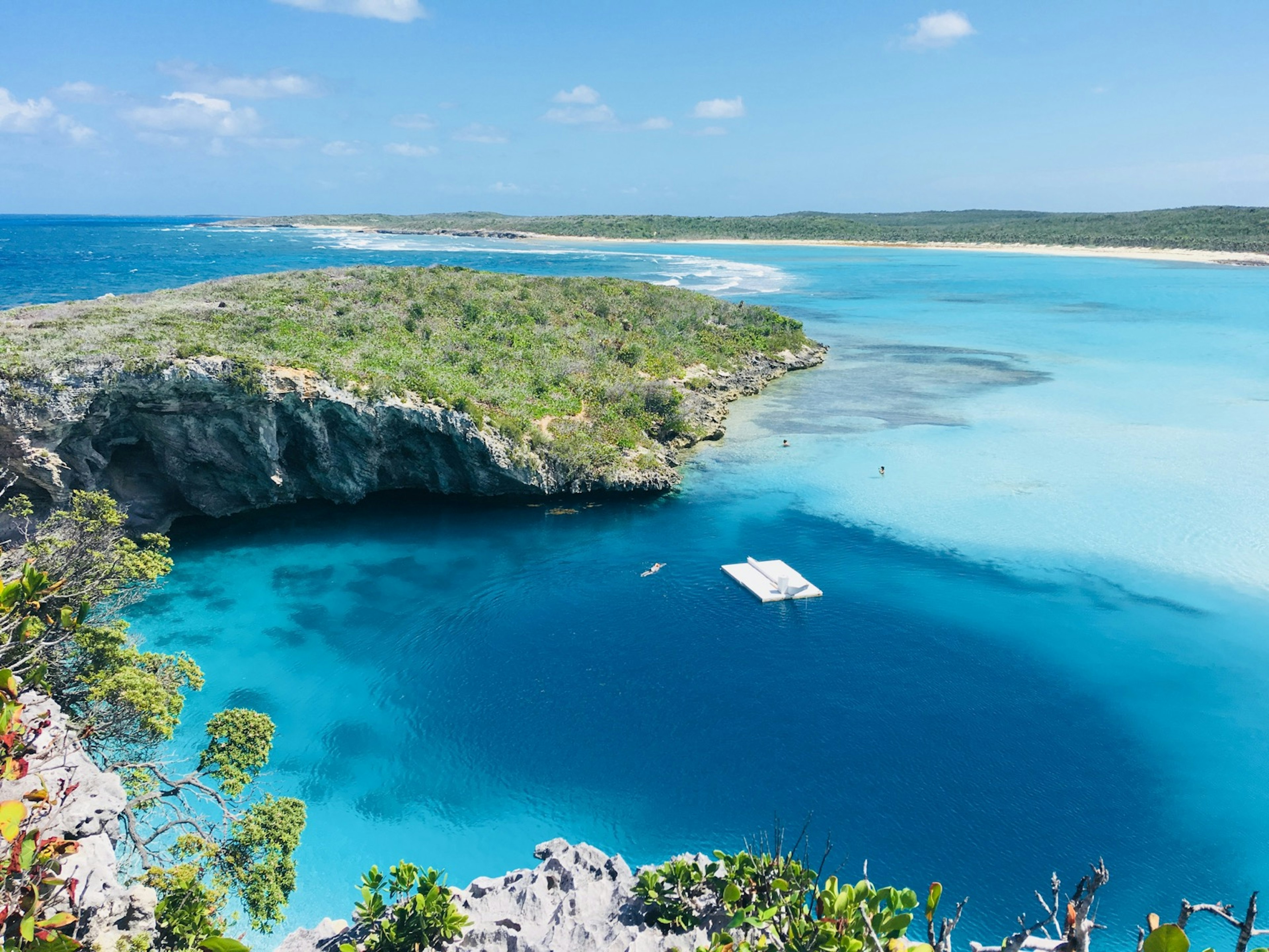 An aerial view of Dean's Blue Hole and the surrounding cliffs. There is a white floating platform in the middle of the water; Long Island Bahamas