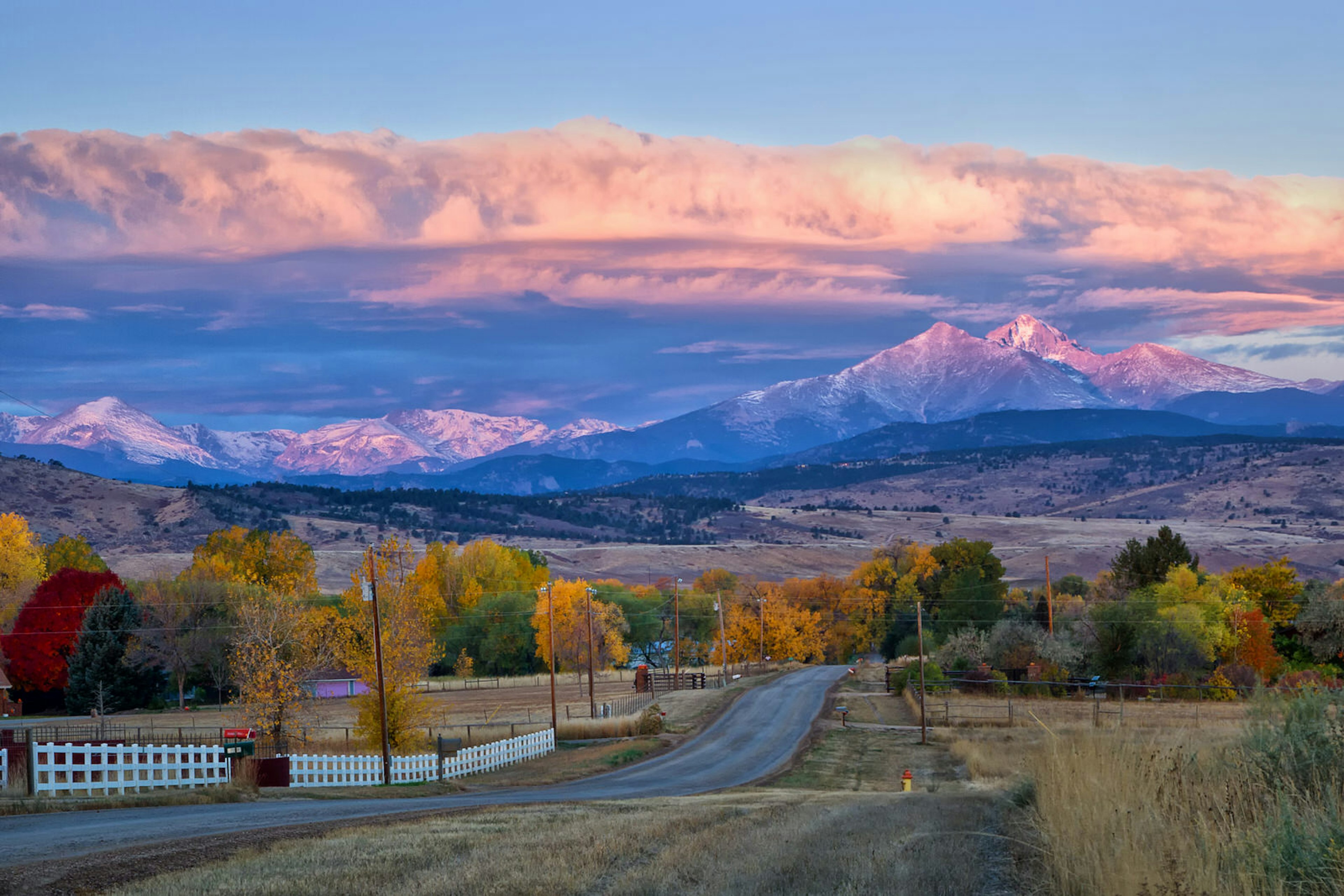 Long's Peak lights up at sunrise as a rural country road leads into the fall trees © Ronda Kimbrow / Getty Images