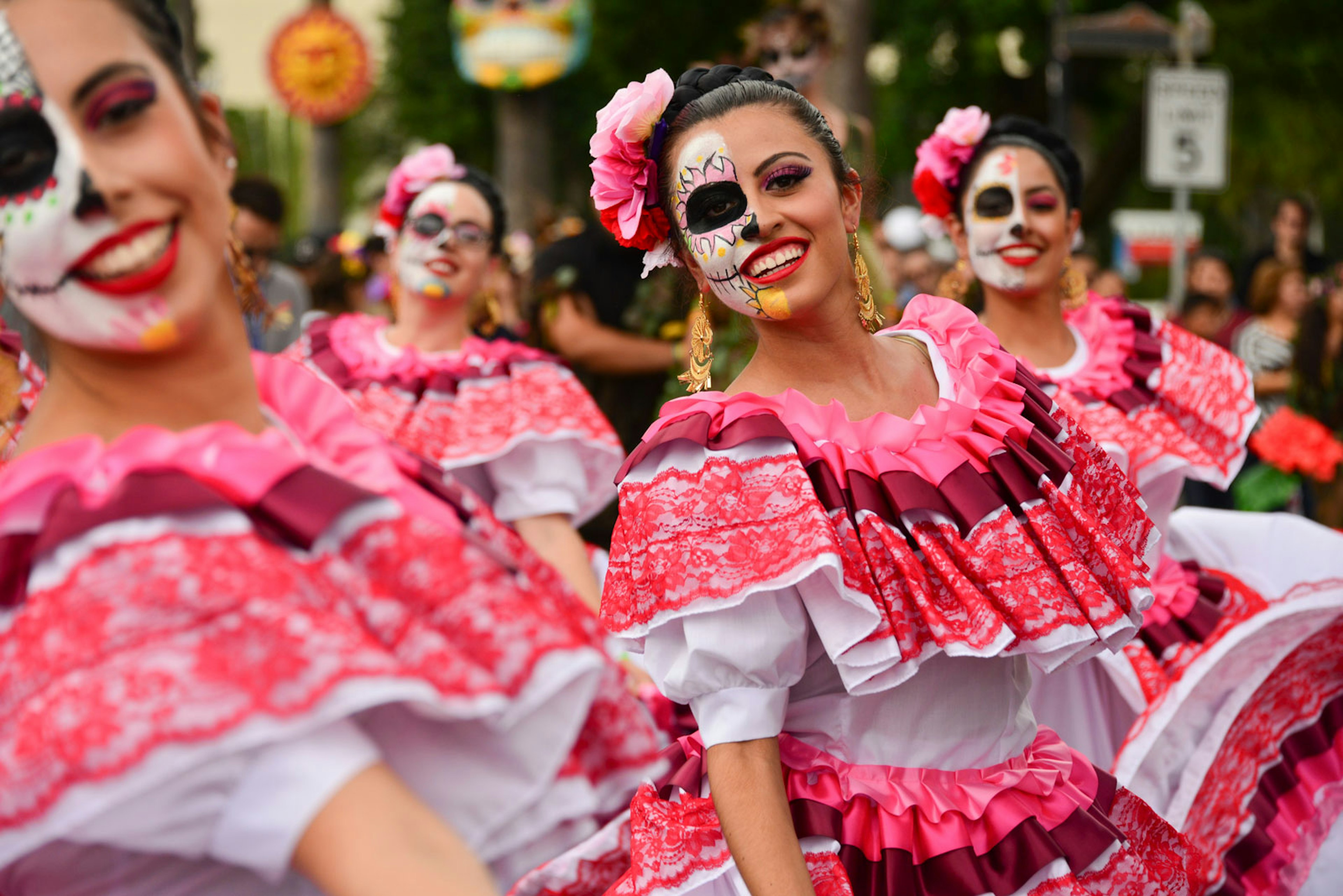 Women dance in pink and red traditional dresses their faces painted in the calavera style