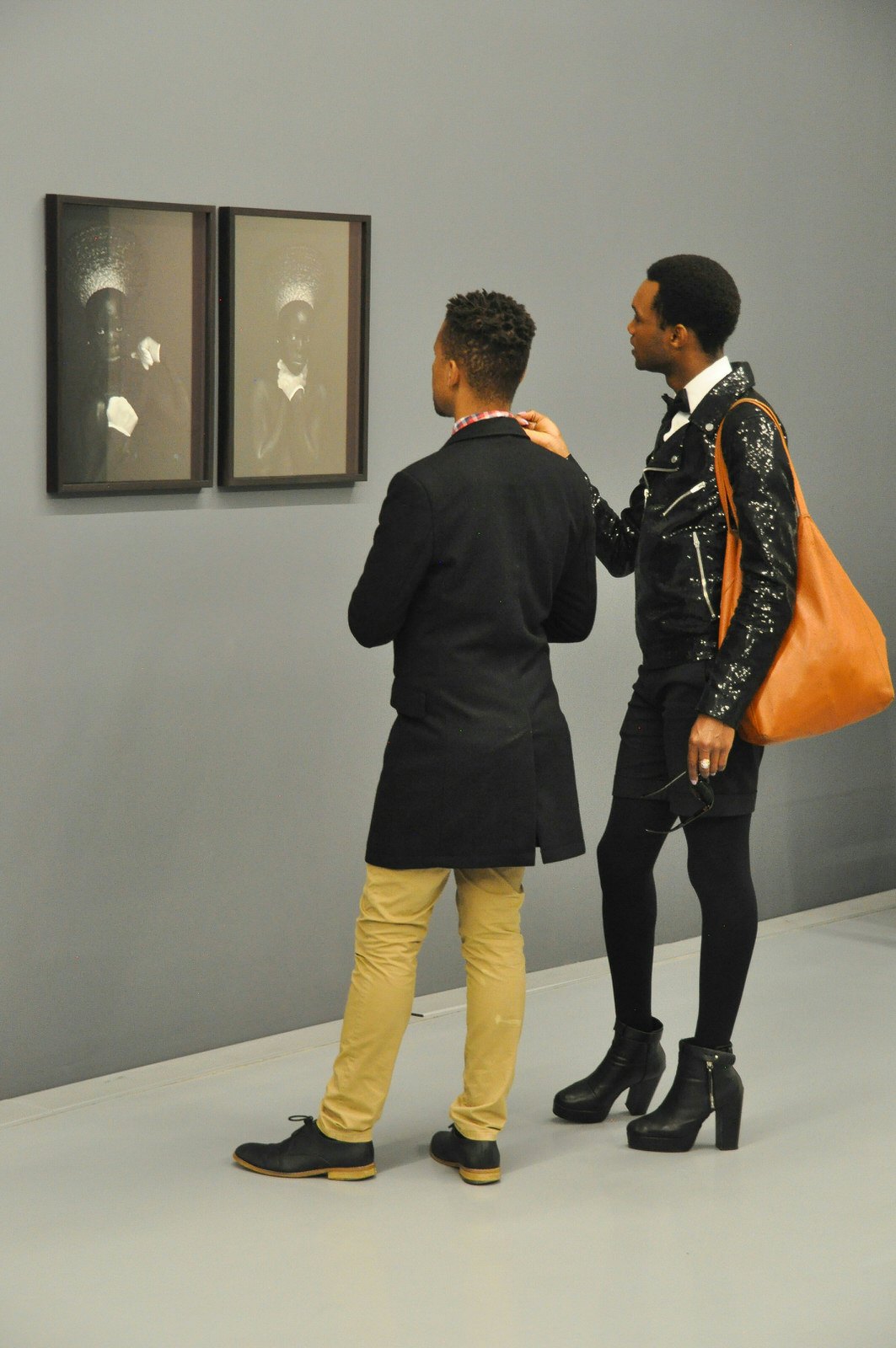 A dark grey wall holds to black-framed black-and-white photographs of an African woman. Two men stand in front of them, clearly engaged. © Monica Suma / Lonely Planet