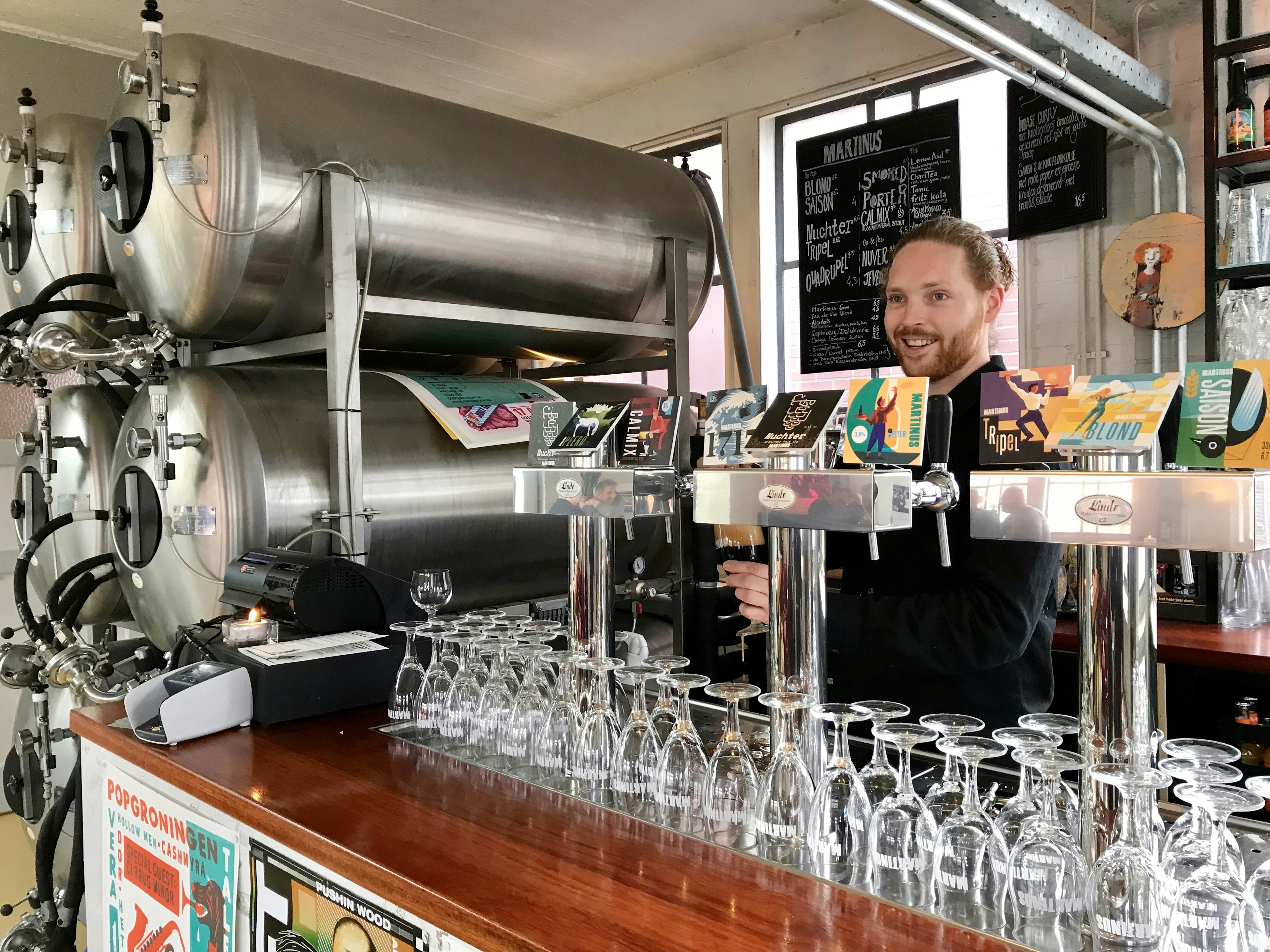 A man pulls a pint behind the bar at Brouwerij Martinus. There are craft brews on tap and large silver stills tucked next to the bar © Sara van Geloven/ϰϲʿ¼