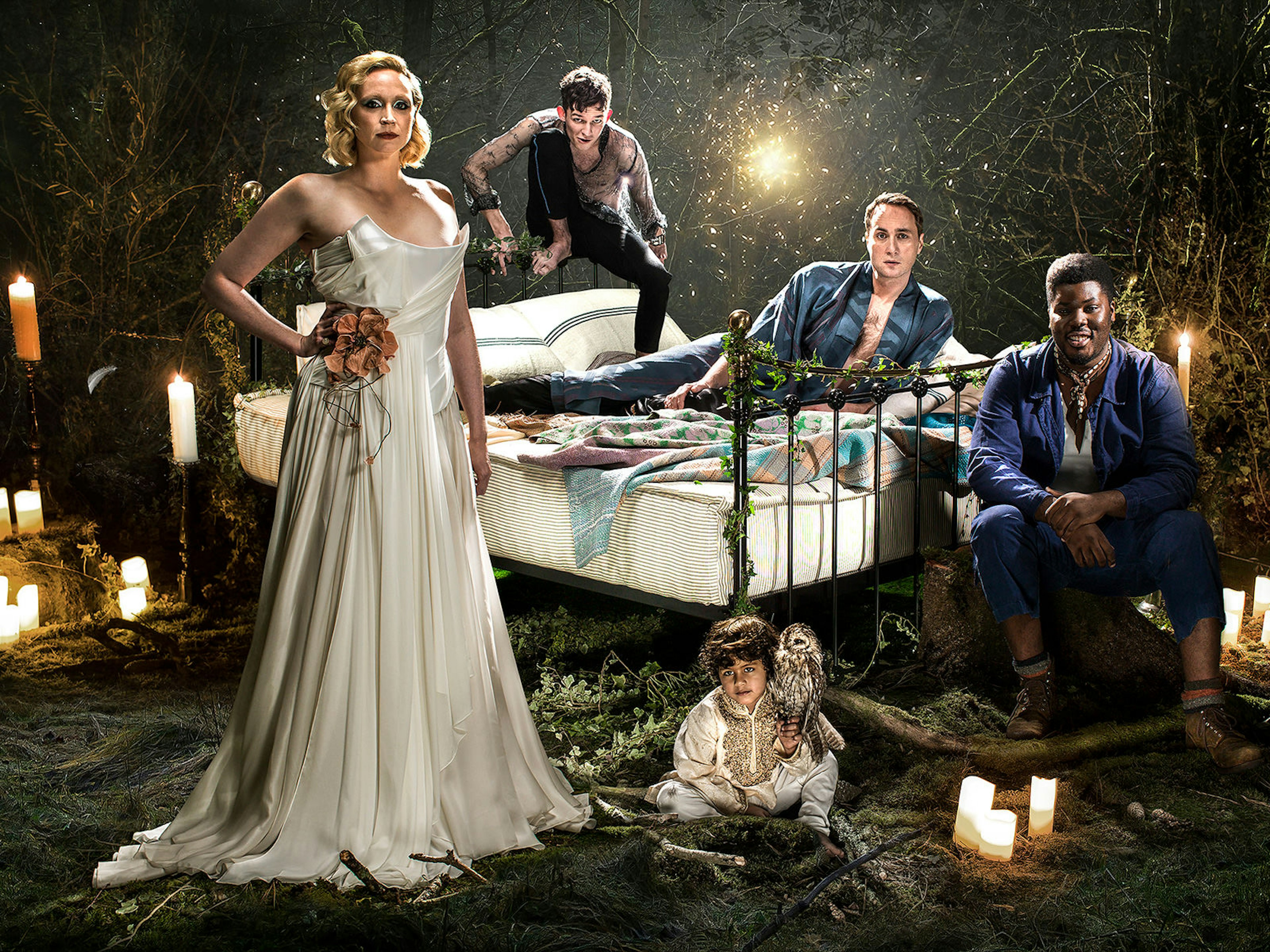 Celebrities West End Braodway - Gwendoline Christie leads the cast of A Midsummer Night's Dream at the Bridge Theatre, London. Gwendoline stands in front of the other cast members, posed around a wrought iron bed, in a floor-length, white silk gown © Perou