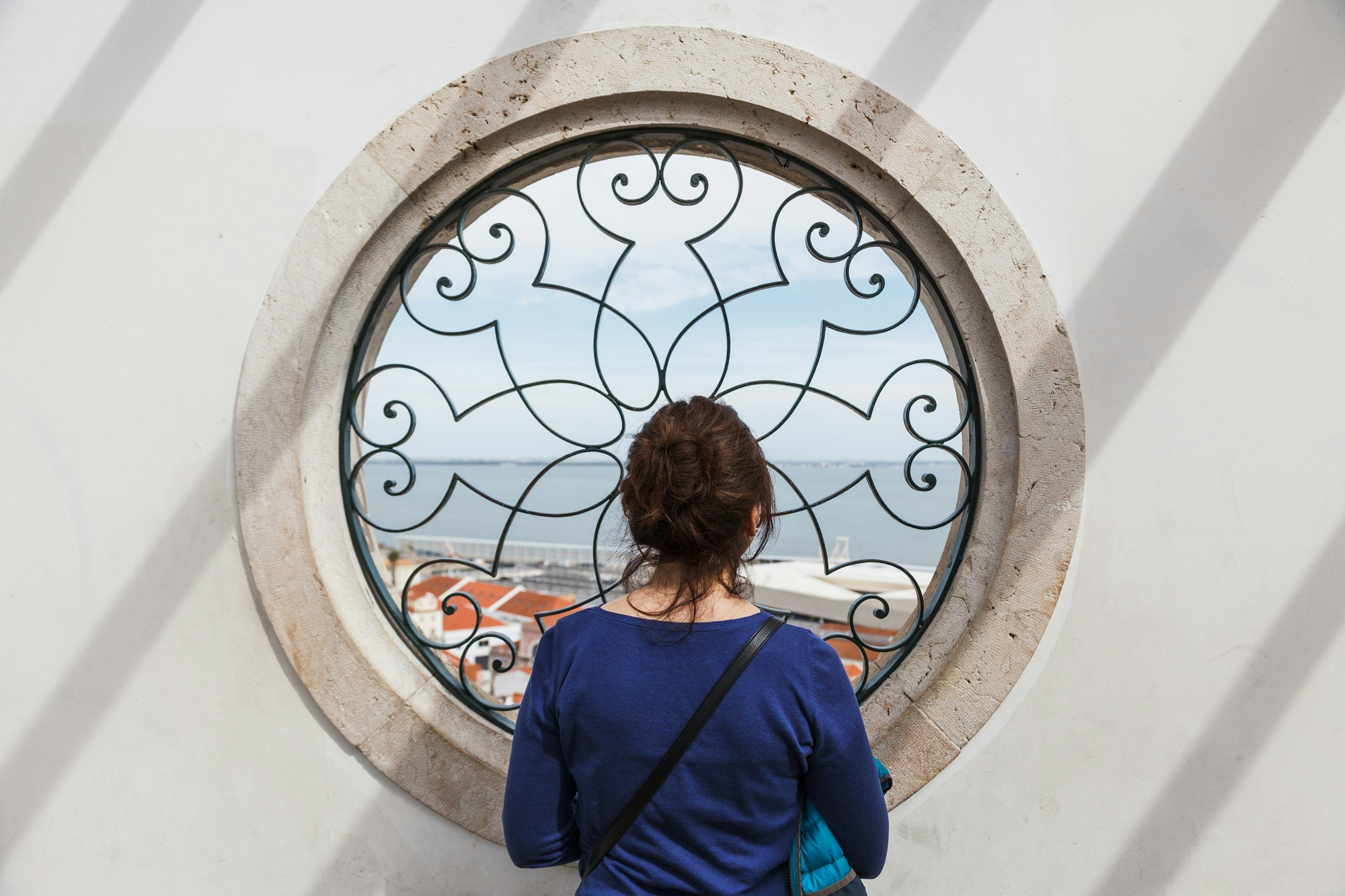 A woman stands with her back to the camera and peers through Miradouro de Santa Luzia in Lisbon, Portugal