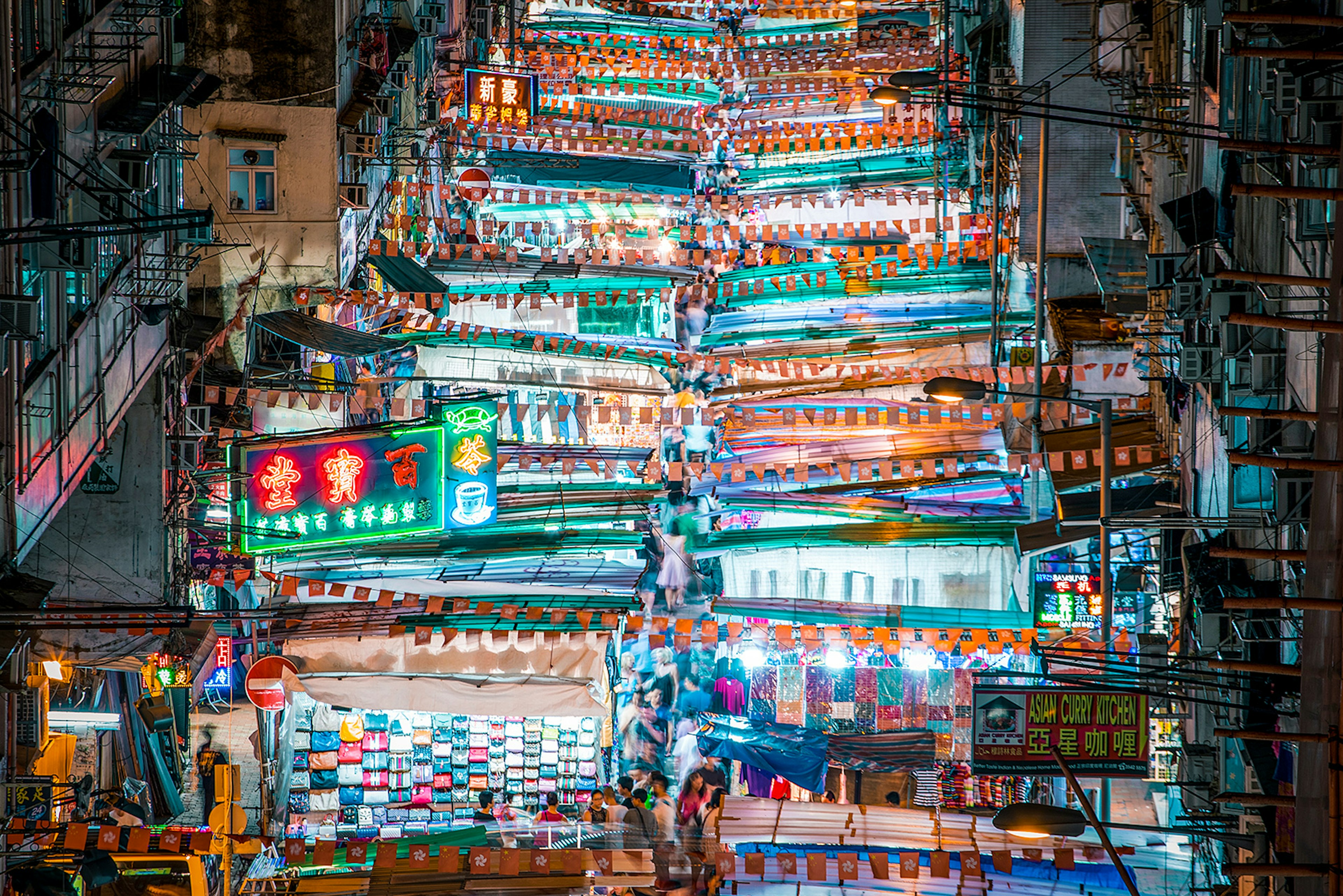 An overhead shot of numerous brightly lit shopping stalls in a street market in Mong Kok, Hong Kong.