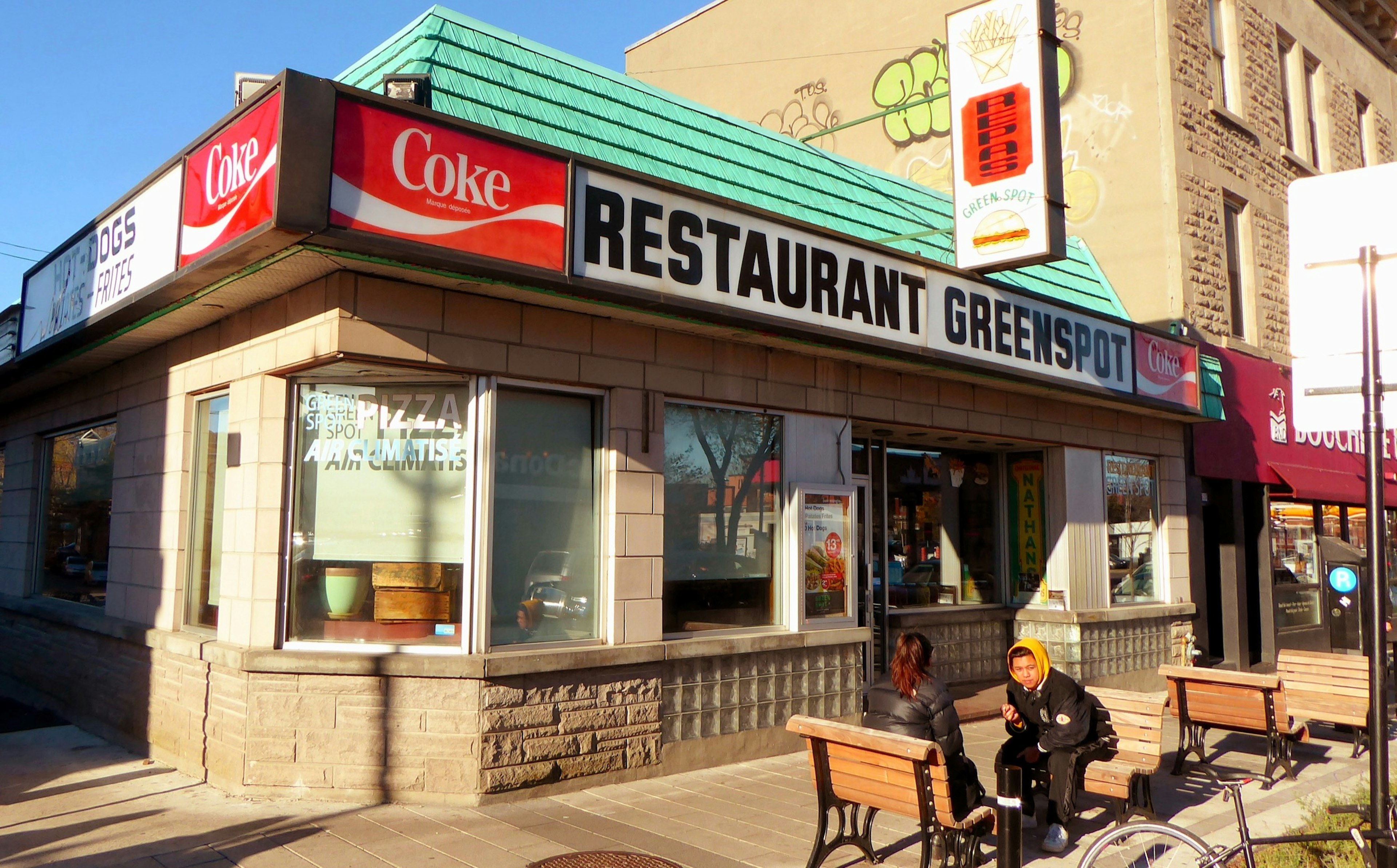 The facade of a small restaurant called the Greenspot is seen, with two bundled-up people sitting outside; fall in Montreal