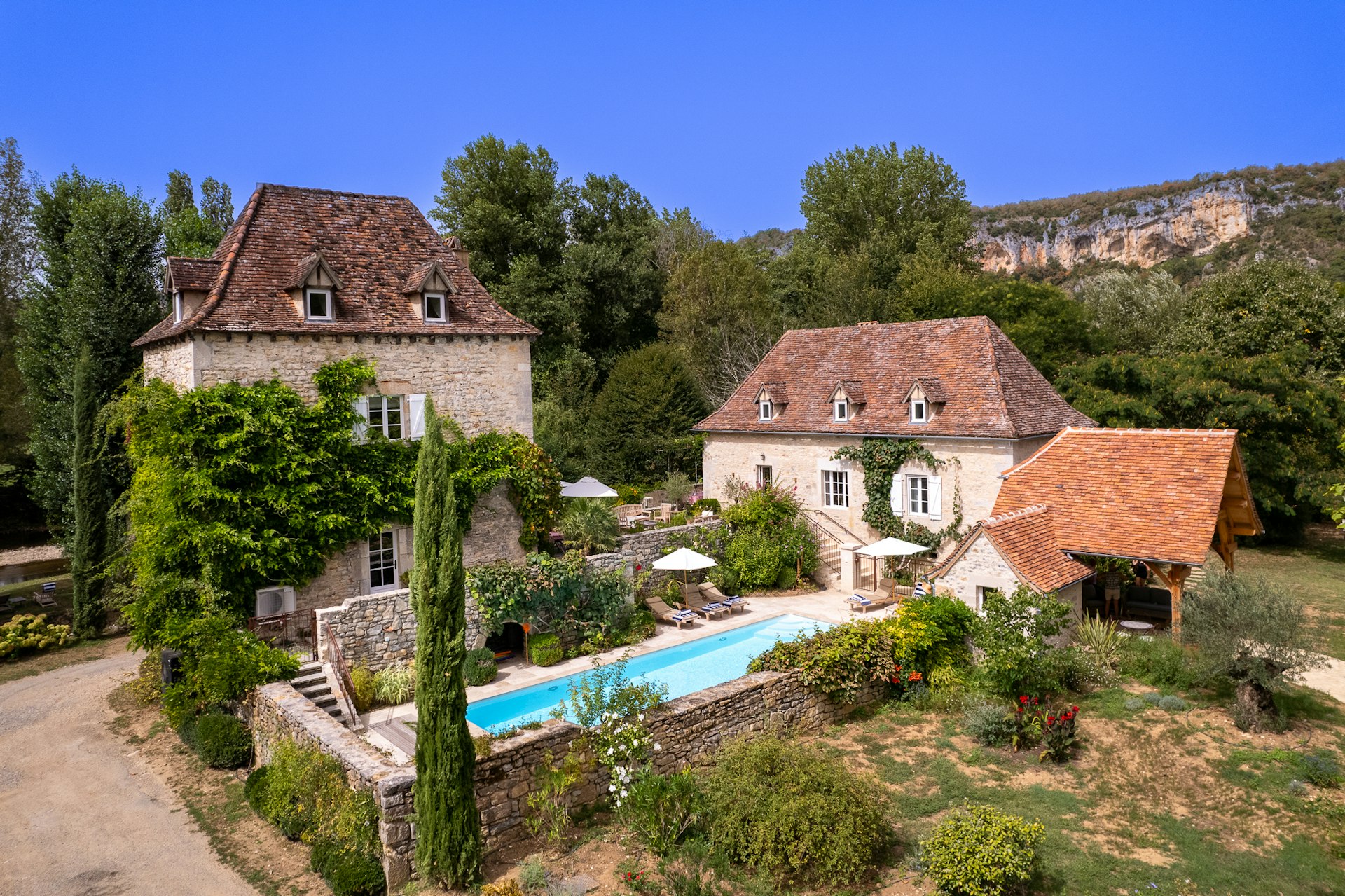 A large property in the countryside with a blue swimming pool sheltered by stone walls