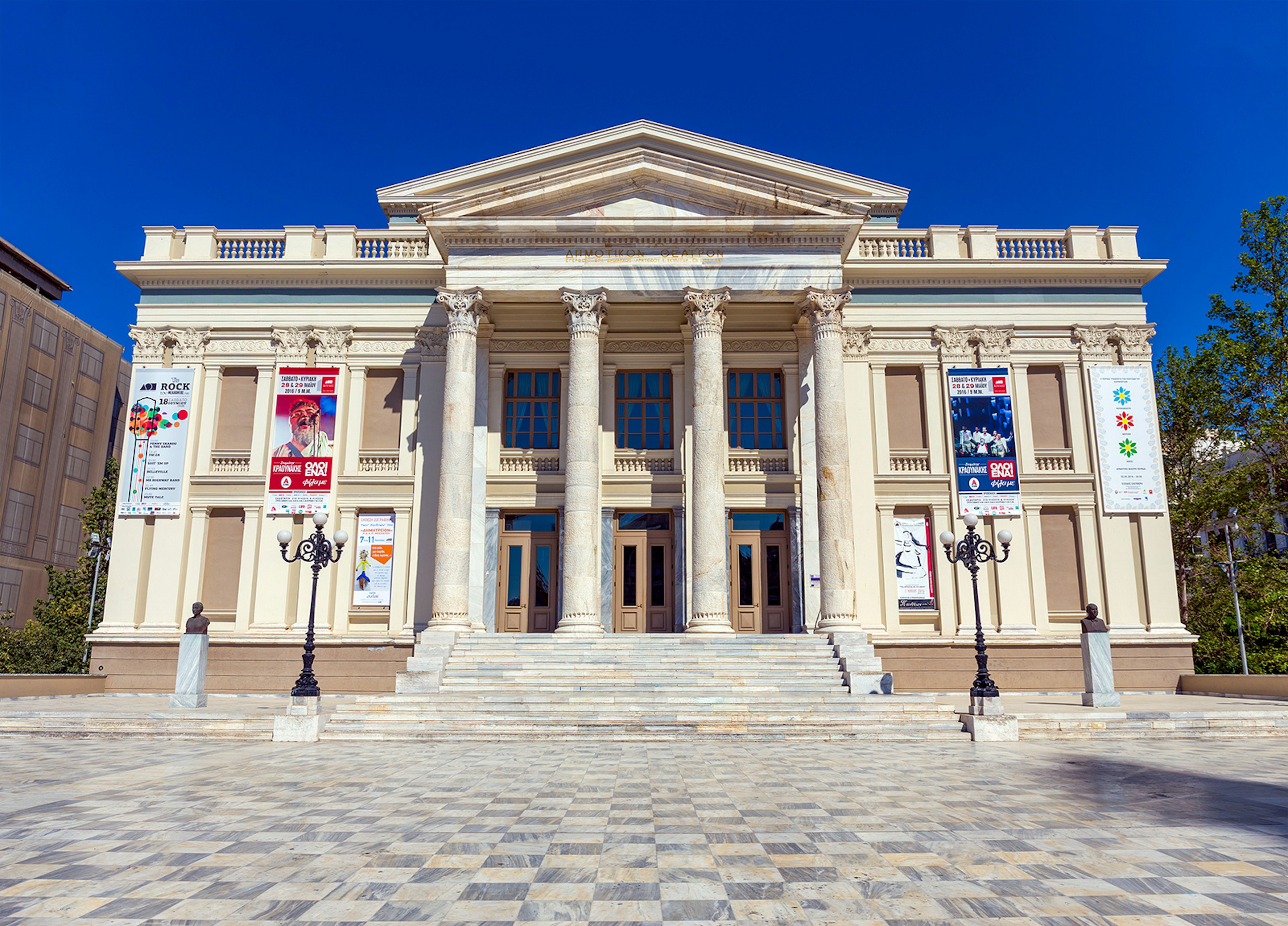 A neoclassical theater house sits in a plaza with checked stones. Piraeus, Greece.