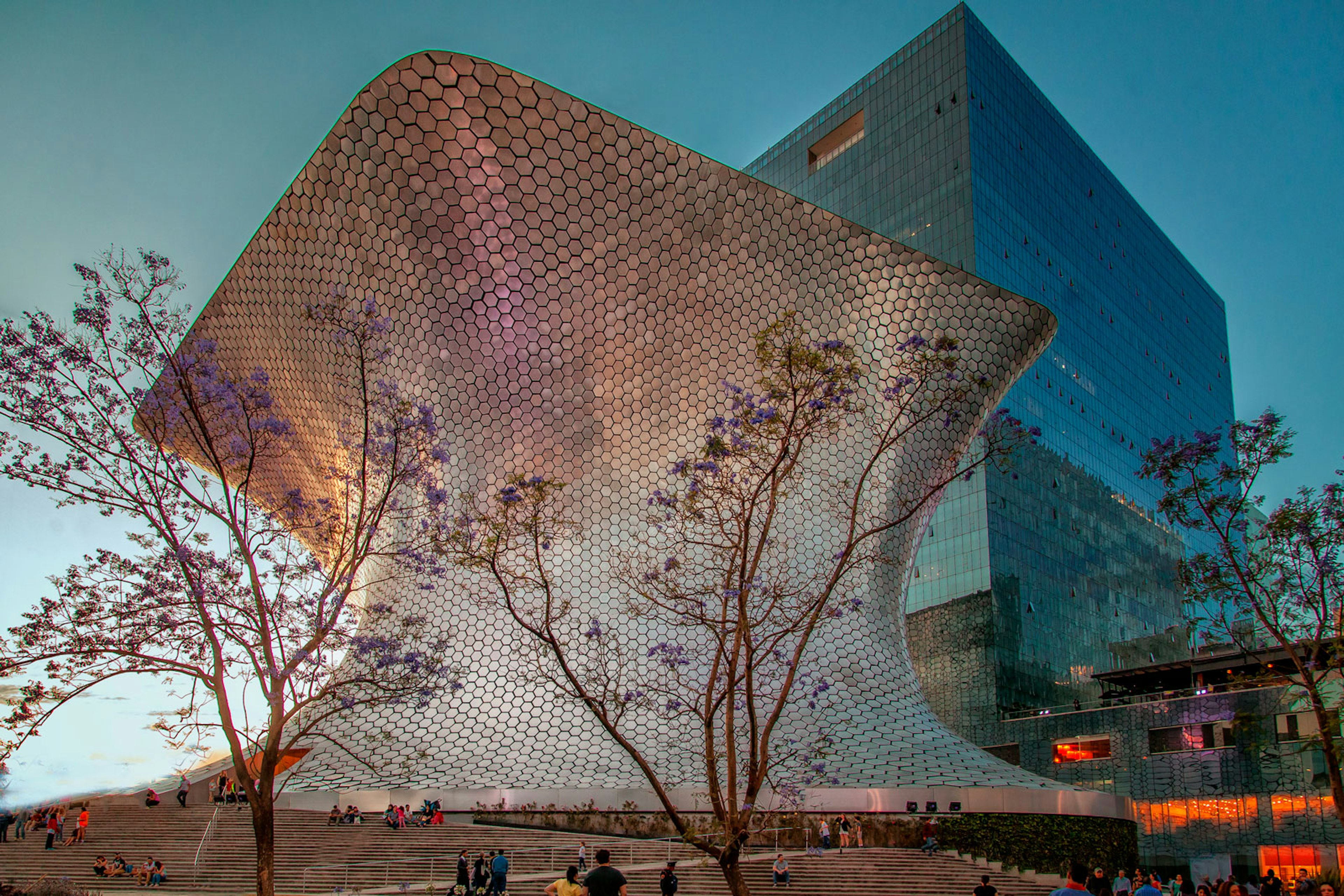 A large building covered in 16,000 hexagonal silver tiles turns slightly purple in the sunset light