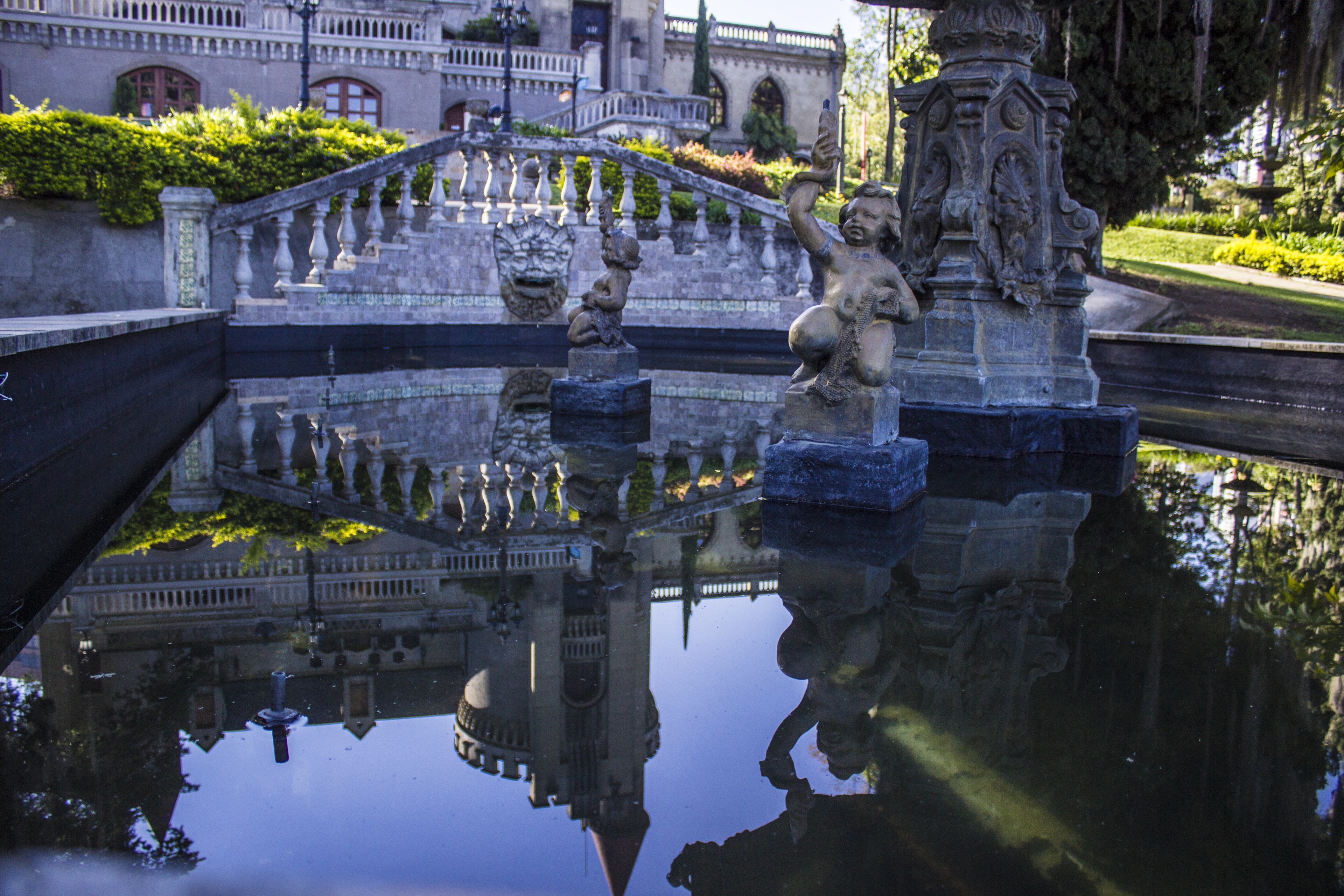 A large fountain with a pair of small cupid sculptures in the middle is positioned in front of the Museo el Castillo in Medellin.