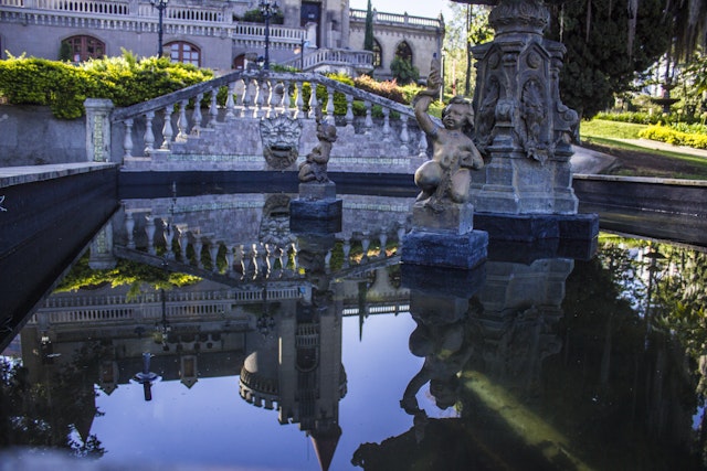 A large fountain with a pair of small cupid sculptures in the middle is positioned in front of the Museo el Castillo in Medellin.