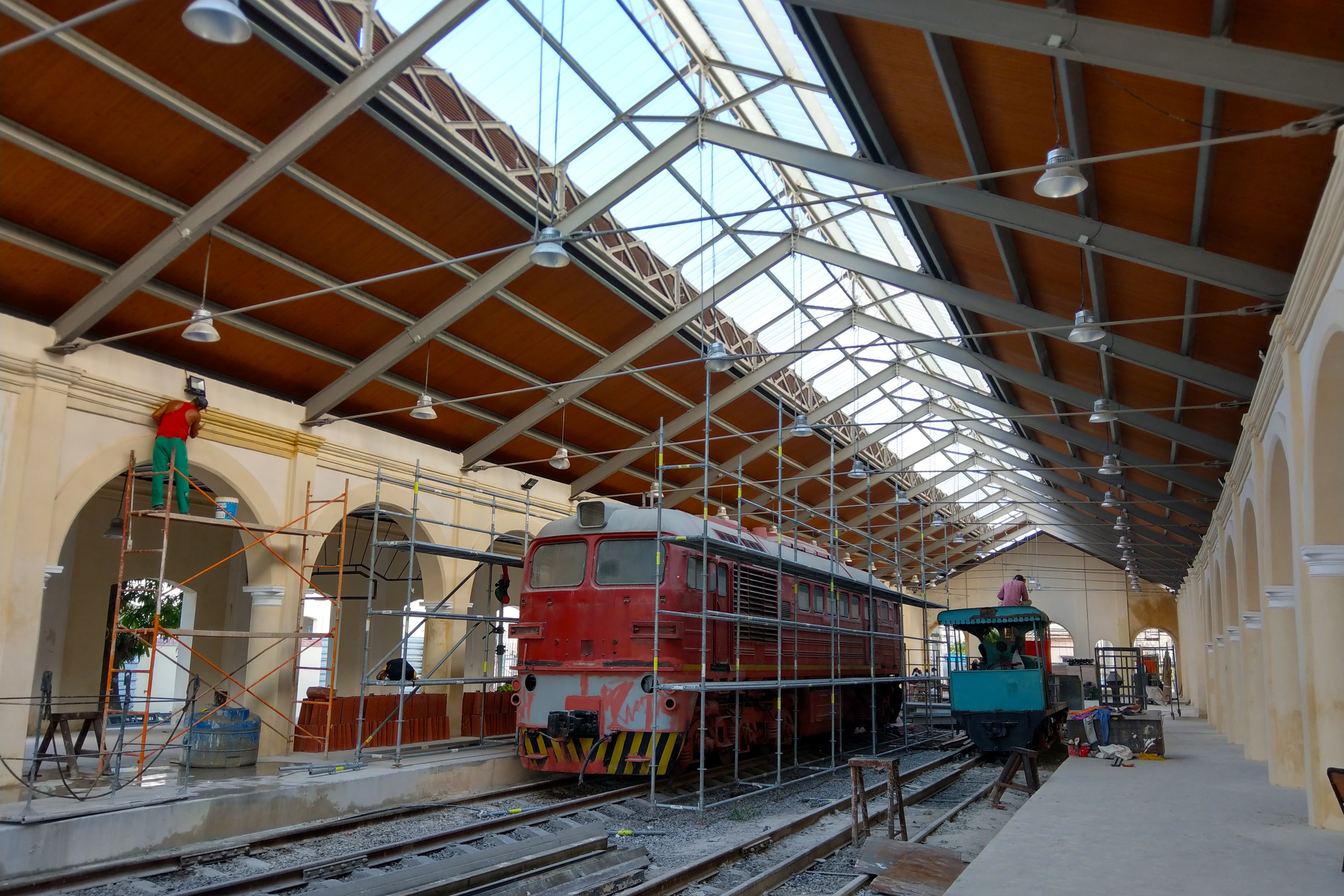 Scaffolding surrounds an old locomotives in an old train station in Havana, In the background, men work on the interior of the train station; Historic Havana sites