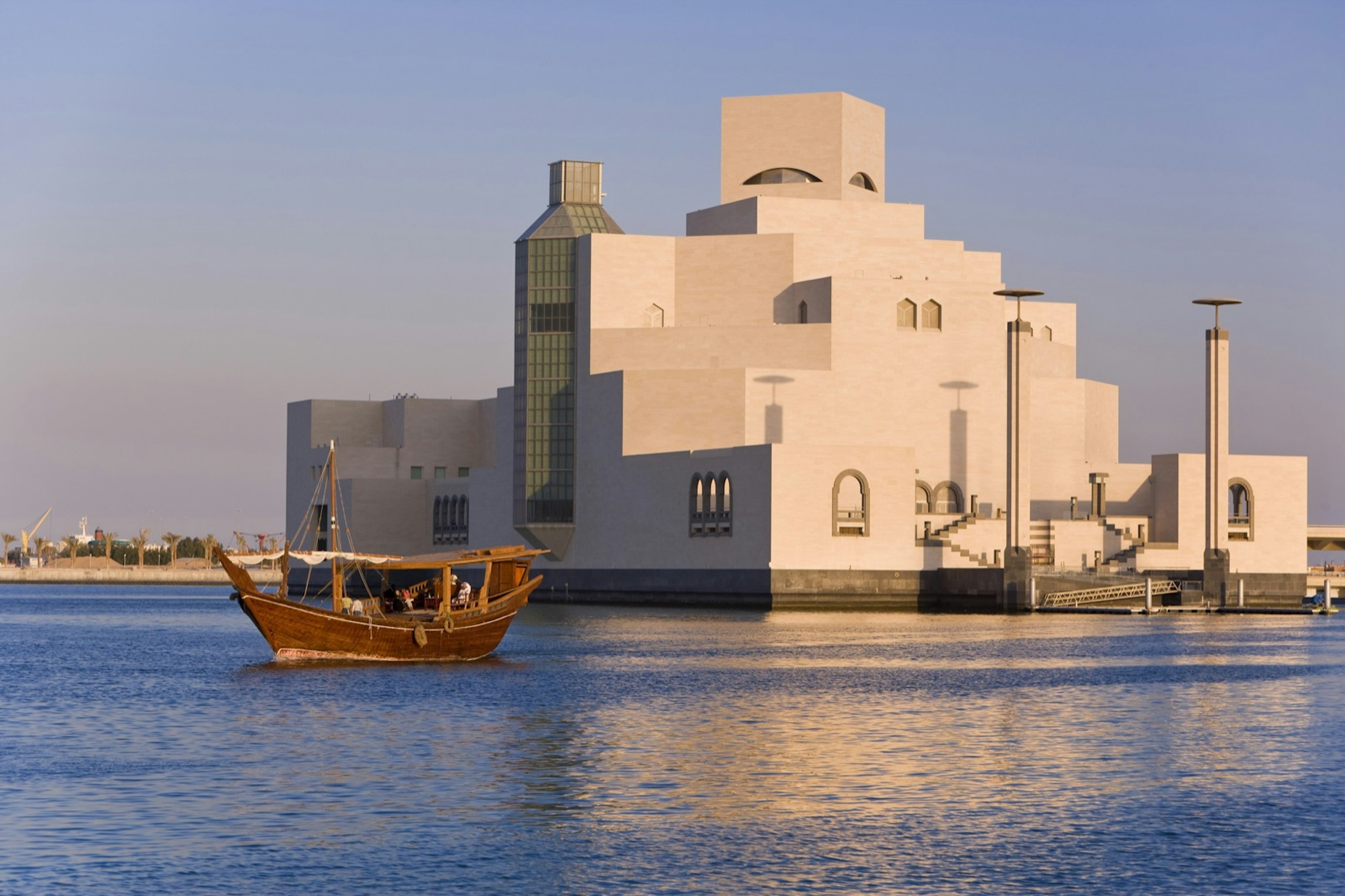 The white cubic structure of the museum grows out of an island with a boat in the forefront