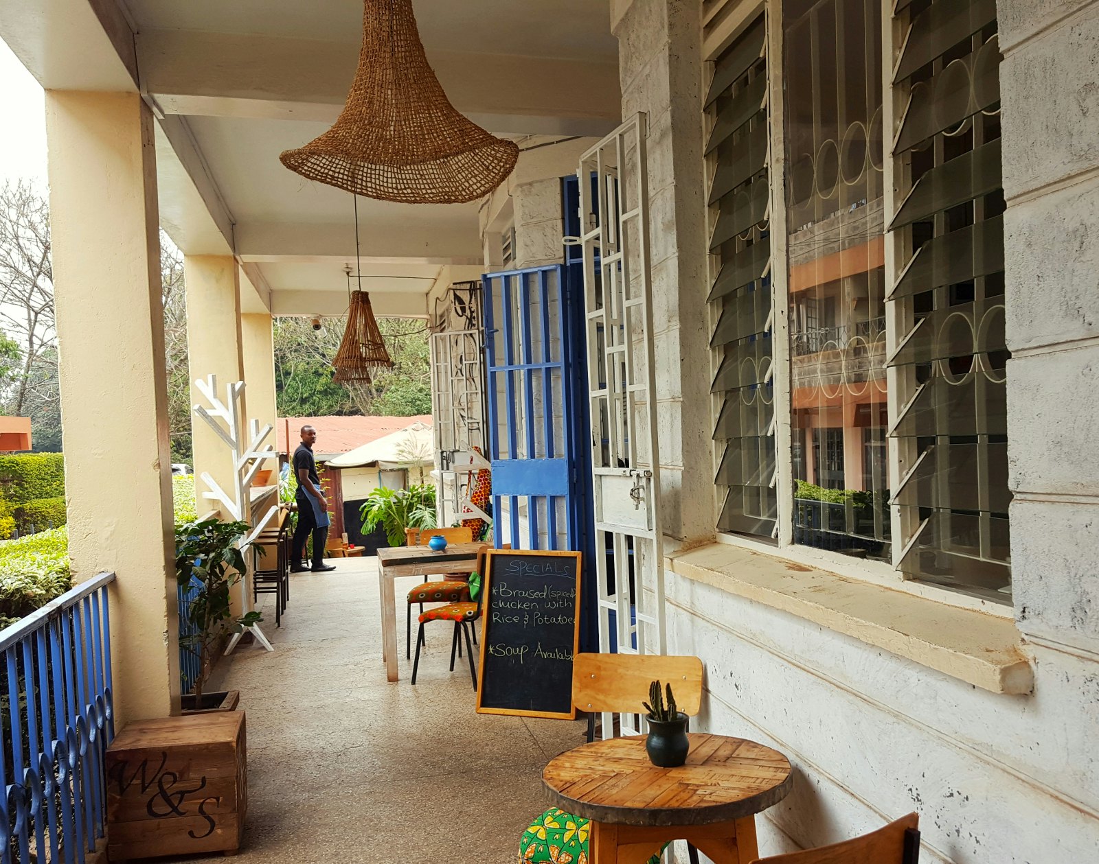 An image looking down the verandah of the Wasp and Sprout cafe. Little wooden tables and chairs sit on one side, with wicker lamp shades above. © Clementine Logan / Lonely Planet