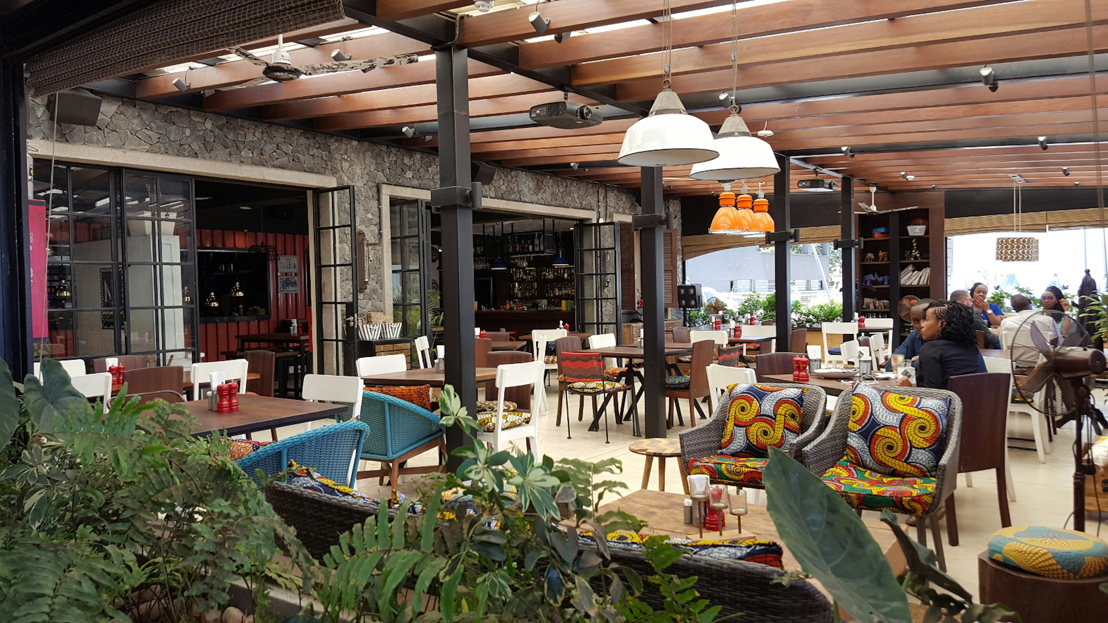 An interior image of the restaurant Nyama Mama in Westlands. It's sunfilled, with wicker chairs of different colours. Steel beams support wooden trestles © Clementine Logan / Lonely Planet