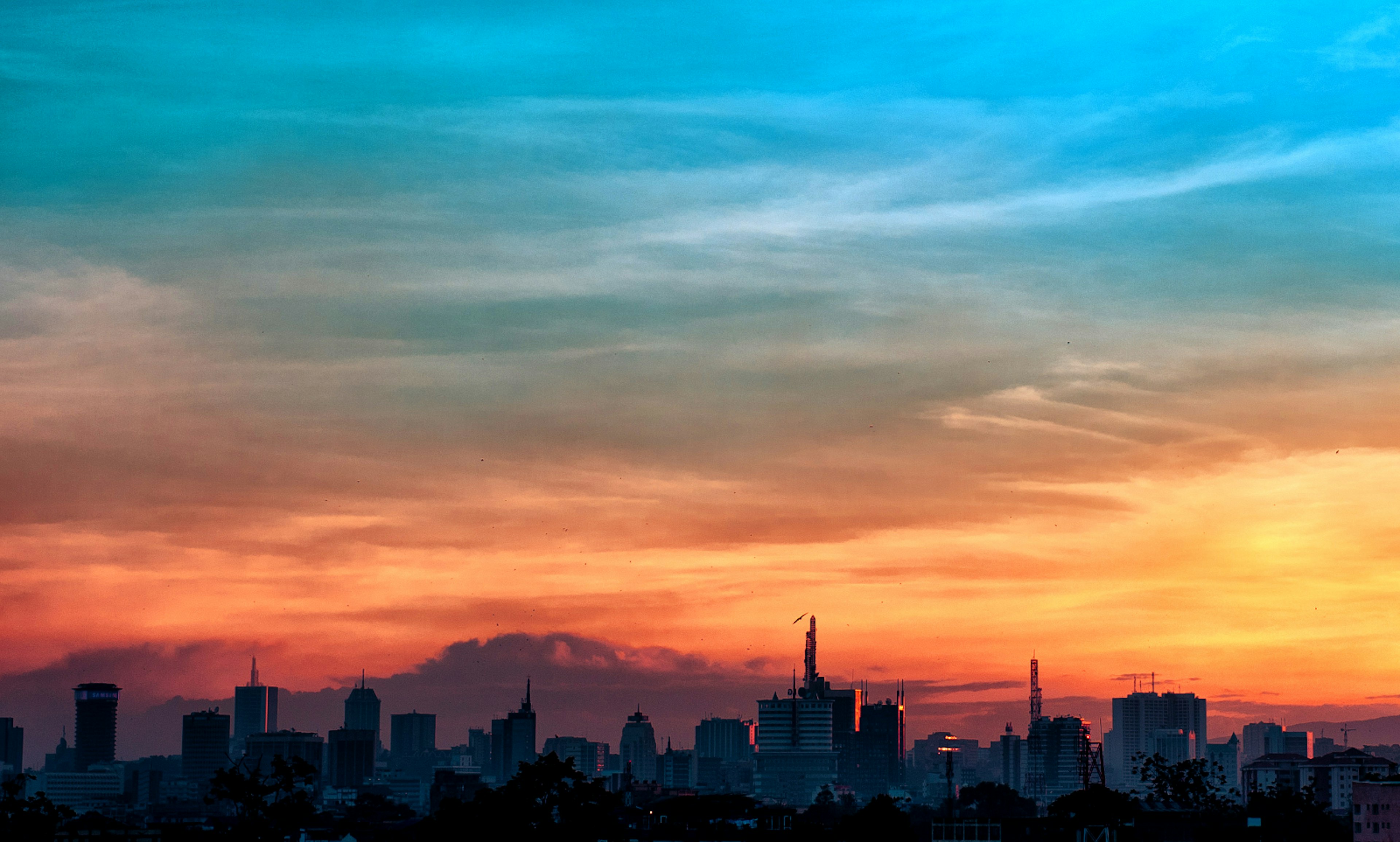 The jagged skyline of Nairobi's high-rises cuts a dark strip below a sky that moves from purple to a bright orage as moving upwards, finishing a bright teal colour ©Jude Gichumbi / 500px