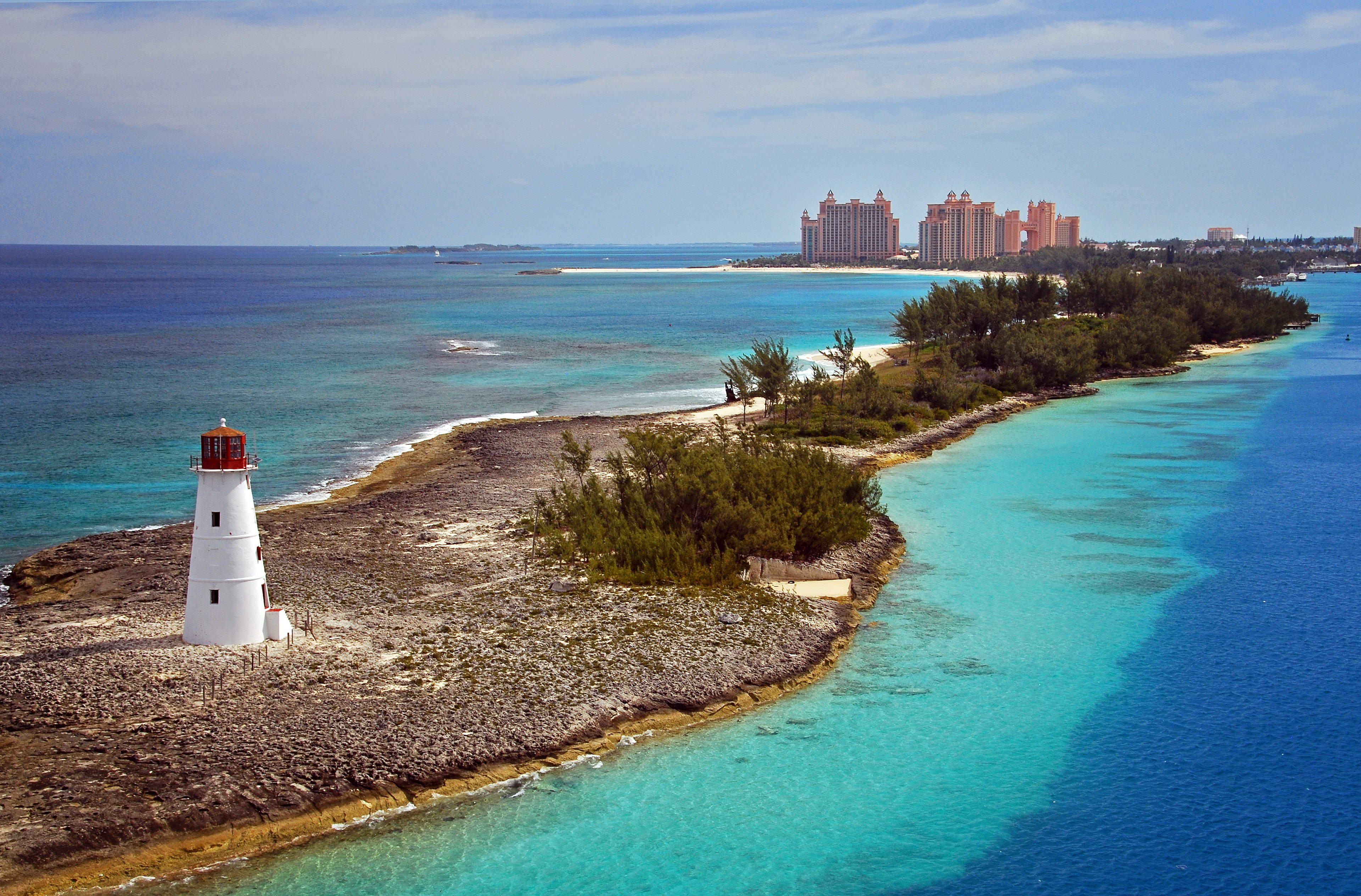 Aerial view of a light house on a rugged shore with overgrown bush. In the distance you can see the Atlantis Resort.