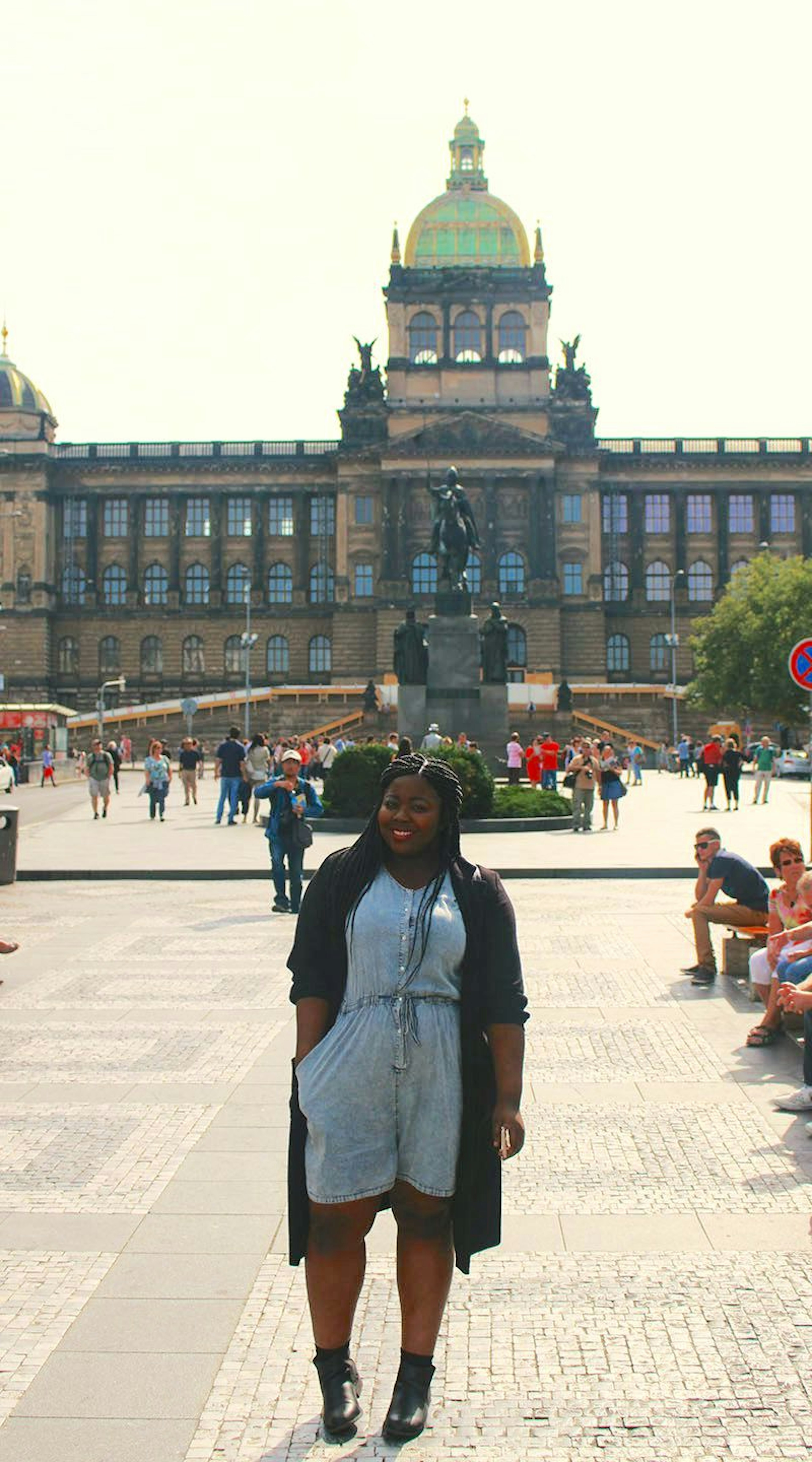 A young black woman smiles for the camera in the sun-dappled square in front of the National Museum in Prague. Black girl travelling tip for Prague, be prepared to see swastikas.