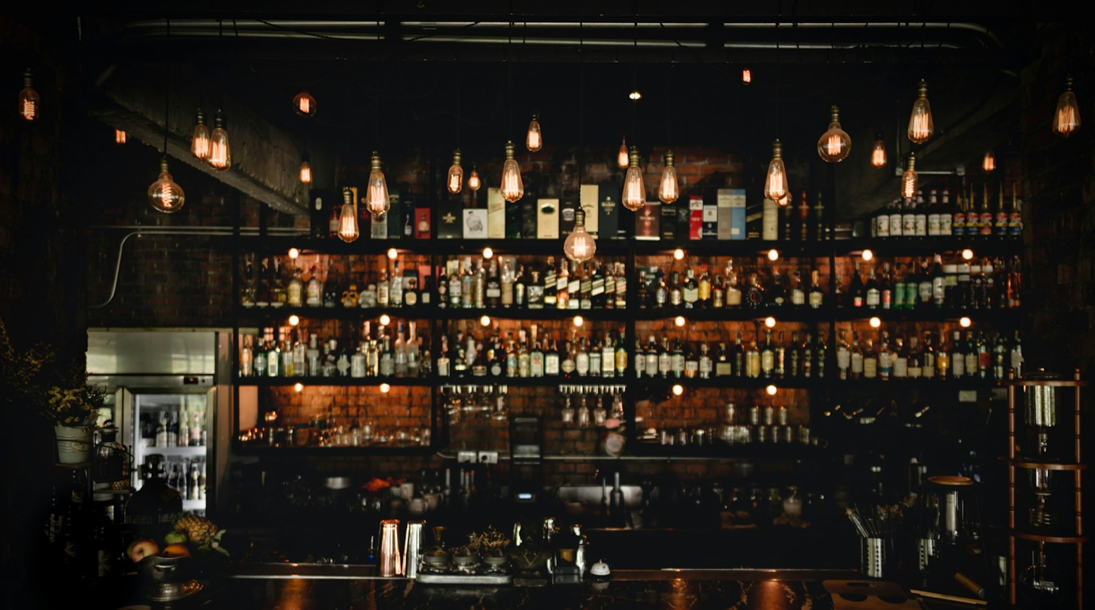 Shelves of bottles are illuminated by vintage lamps in the dark. There are glasses and other mix-drink instruments on the wooden bar. Cocktails can easily play a big role during a New Orleans weekend.